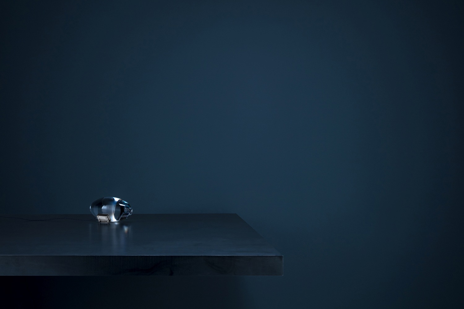 Atman LED Tischleuchte von Catellani & Smith auf dunklem Tisch vor dunkler Wand.