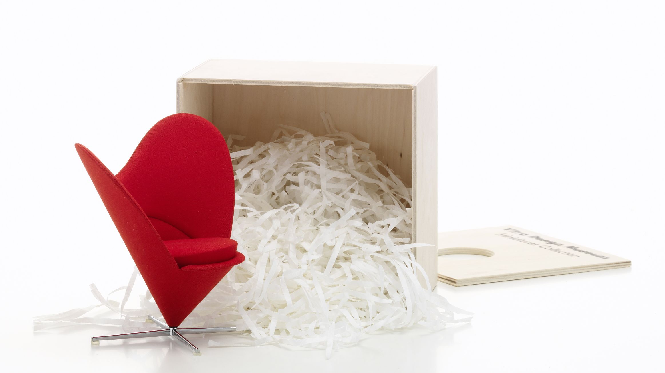 Roter Heart Cone Chair Miniatur Stuhl von Vitra neben einer Holzkiste mit Füllmaterial.