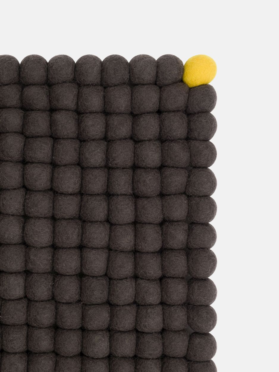 Anthrazitfarbener Filzteppich "Big One" von myfelt (180x260 cm) aus vielen Filzkugeln mit einer gelben Kugel.