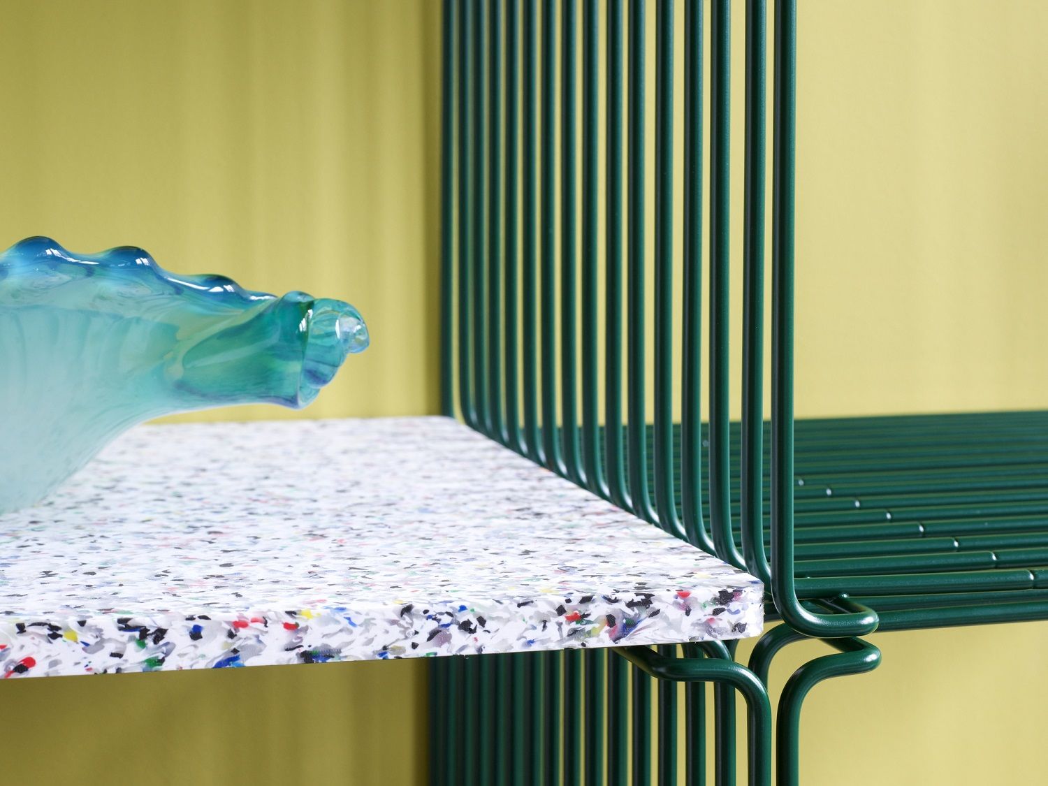 Detailaufnahme: Grünes Montana Wire Cube Regal mit bunter Platte und blauer Glasvase.