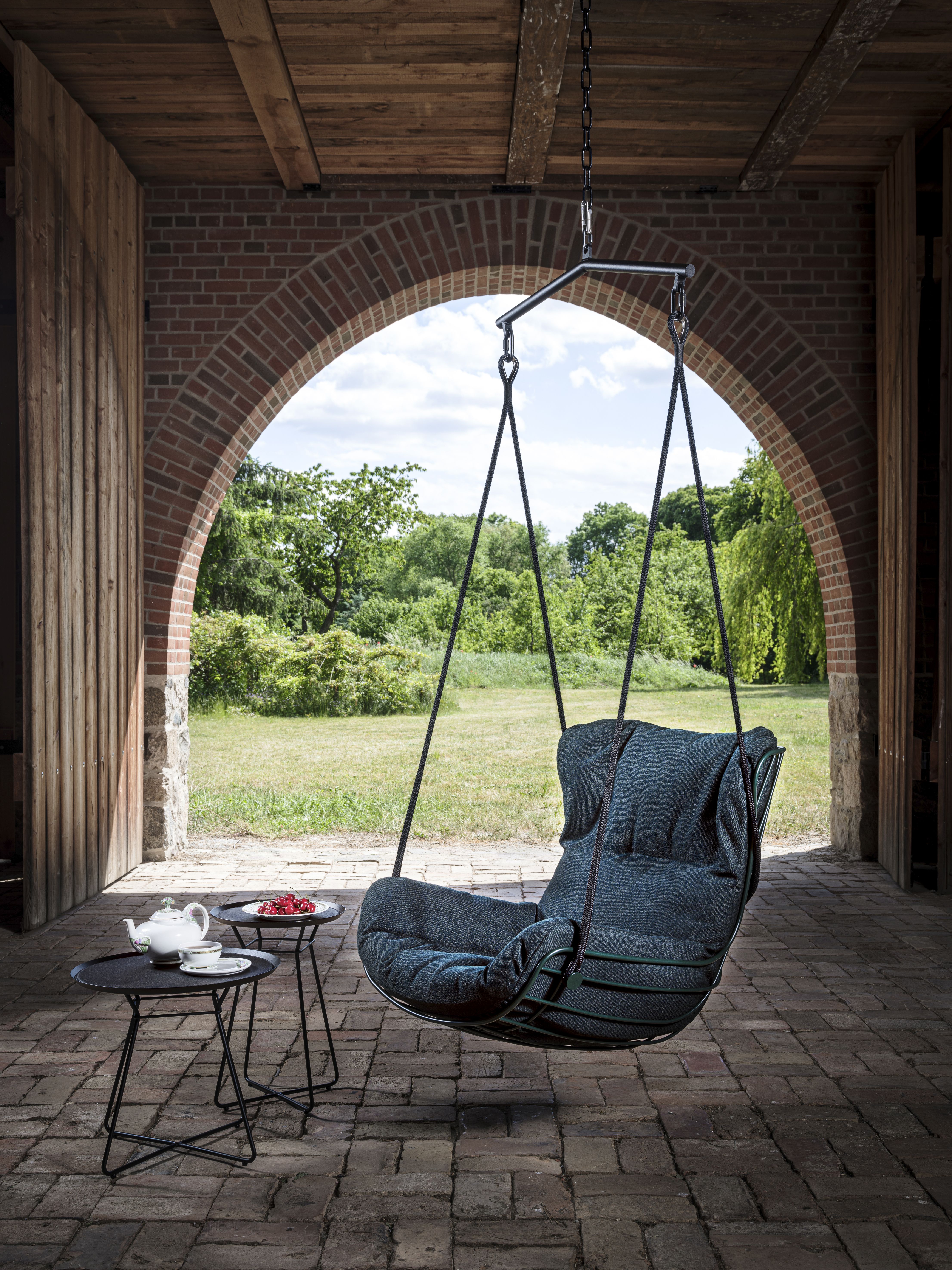 Leyasol Wingback Schwingsessel von Freifrau Manufaktur: Hängesessel mit dunkelblauem Kissen und Teetisch im Freien.
