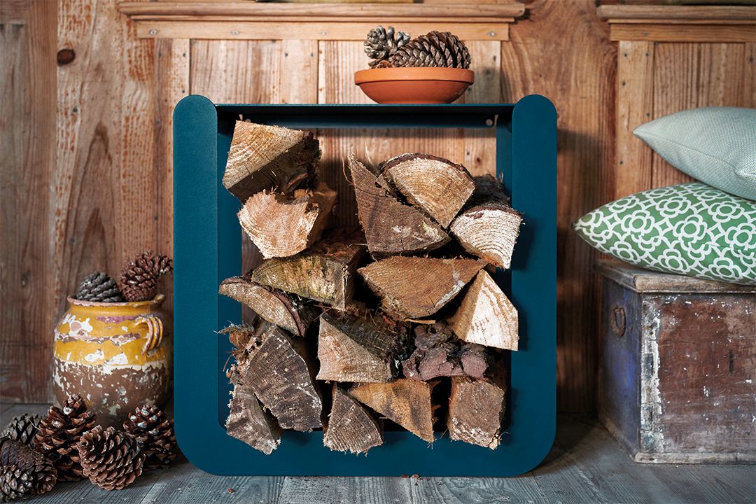 Nevado Holztrage von Fermob, gefüllt mit Brennholz, in einem rustikalen Ambiente mit Holzwand und Dekoration.