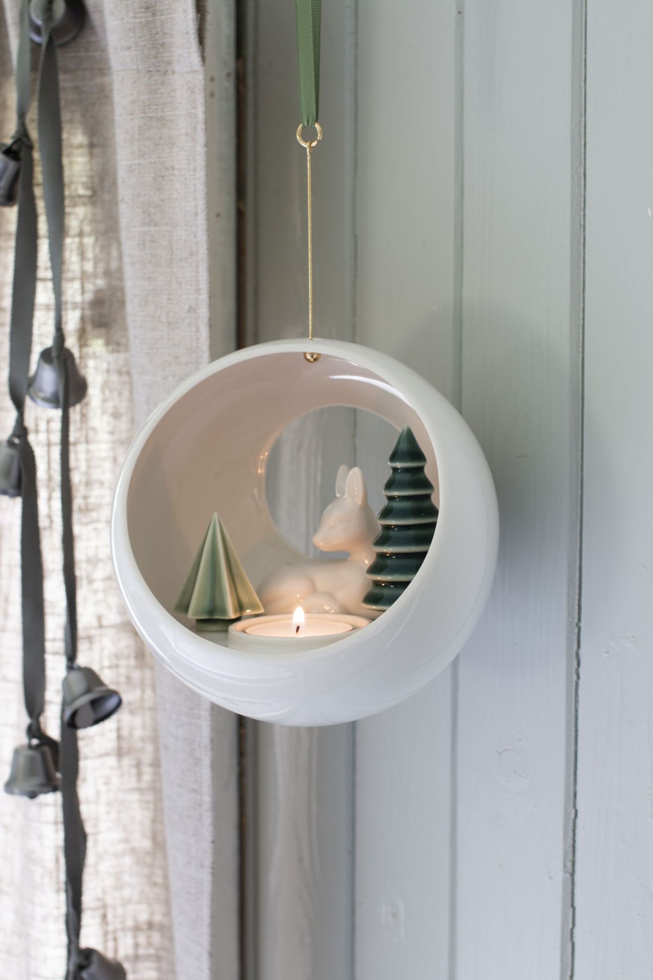 Winterlicher Dottir Teelichthalter mit Rehkitz, Tannenbäumen und brennender Kerze in weißer Keramik-Kugel zum Aufhängen.