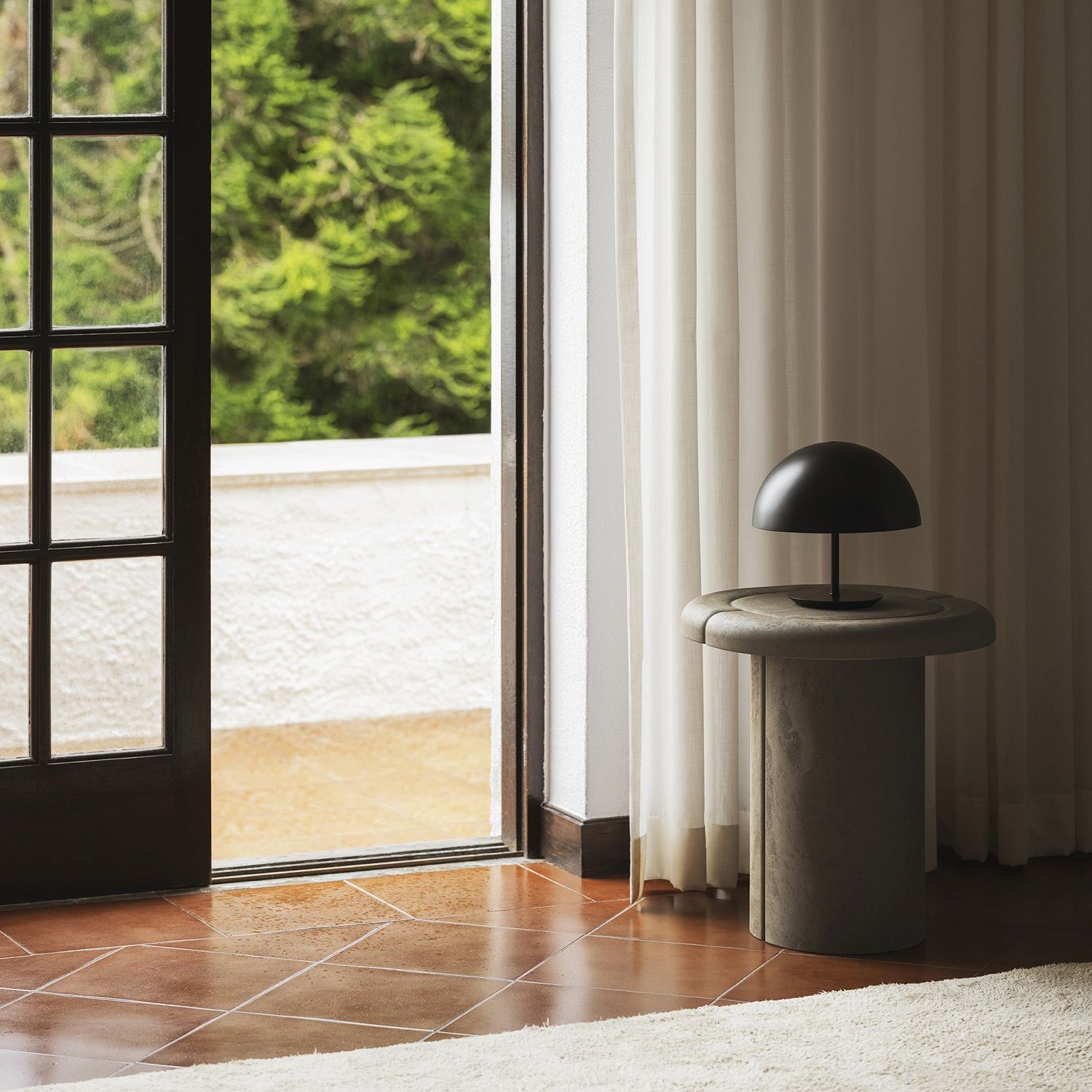 Alder Side Table Beistelltisch von Mater im Innenraum mit Lampe und geöffneter Tür zum Außenbereich.