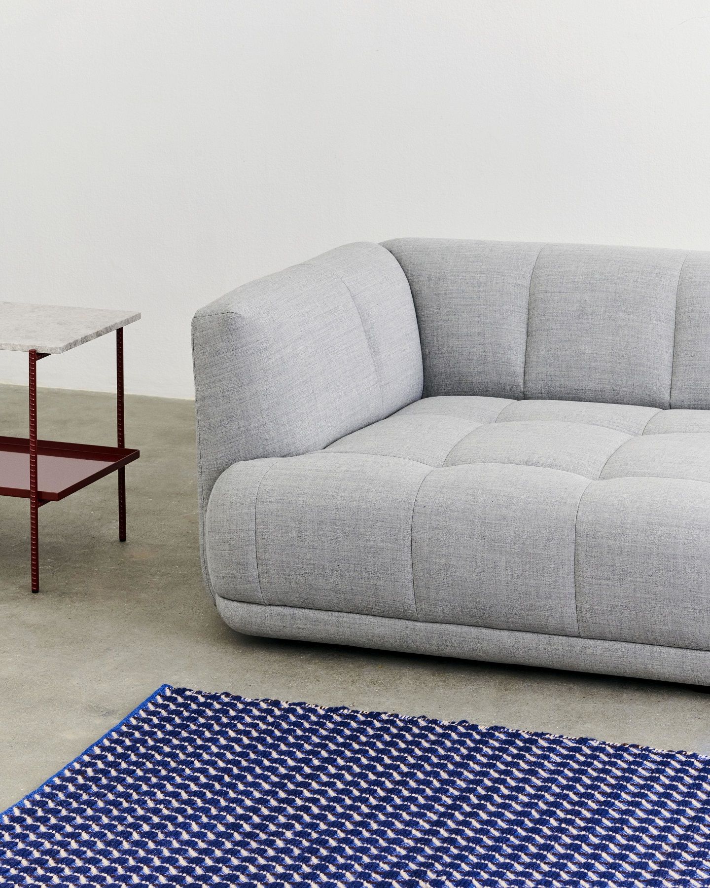 Grauer Rebar Beistelltisch mit Marmorplatte neben einem grauen Sofa und einem blauen Teppich.