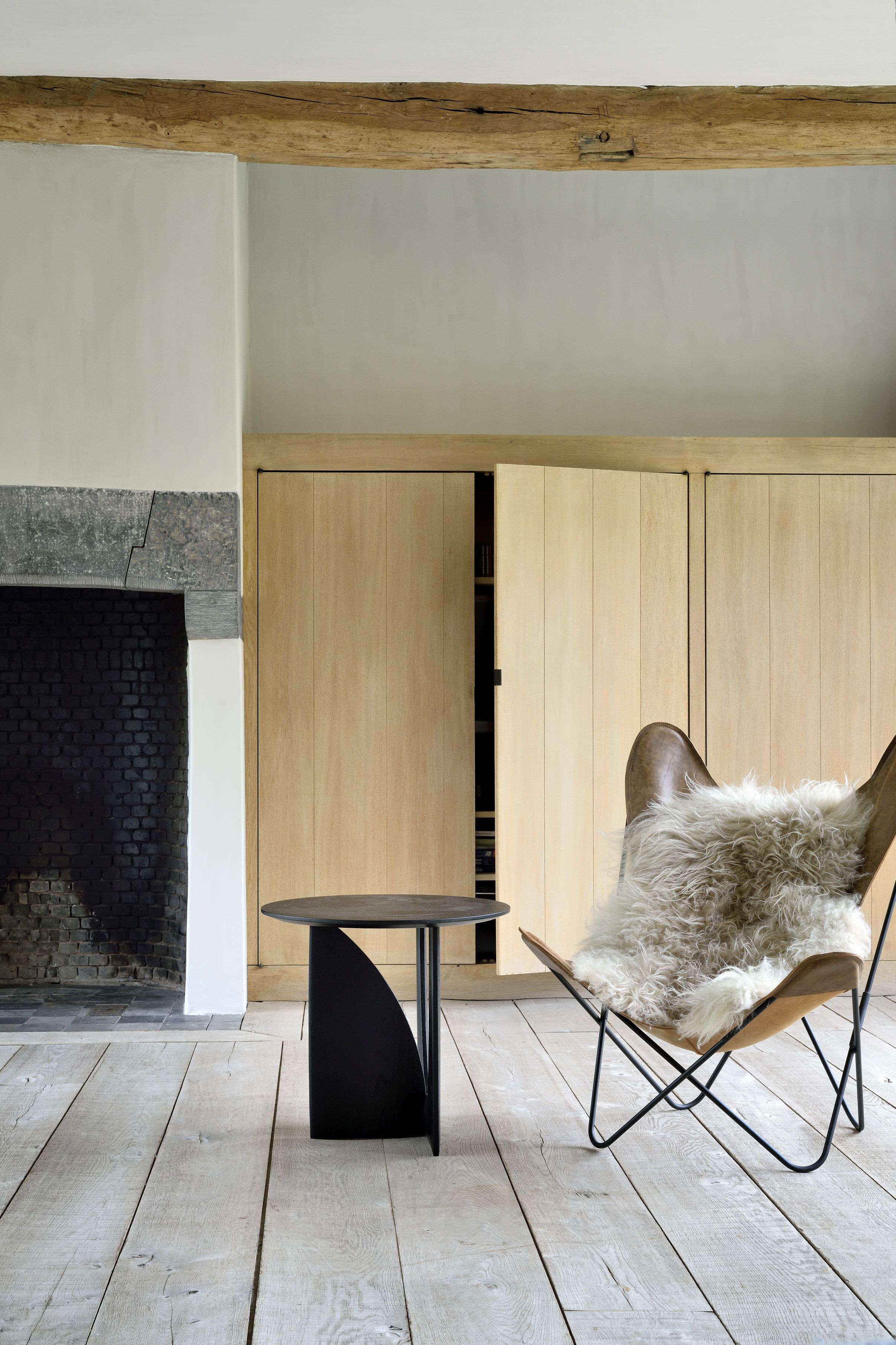 Geometric Beistelltisch Eiche Ethnicraft neben Sessel mit Fell in modernem Wohnzimmer.