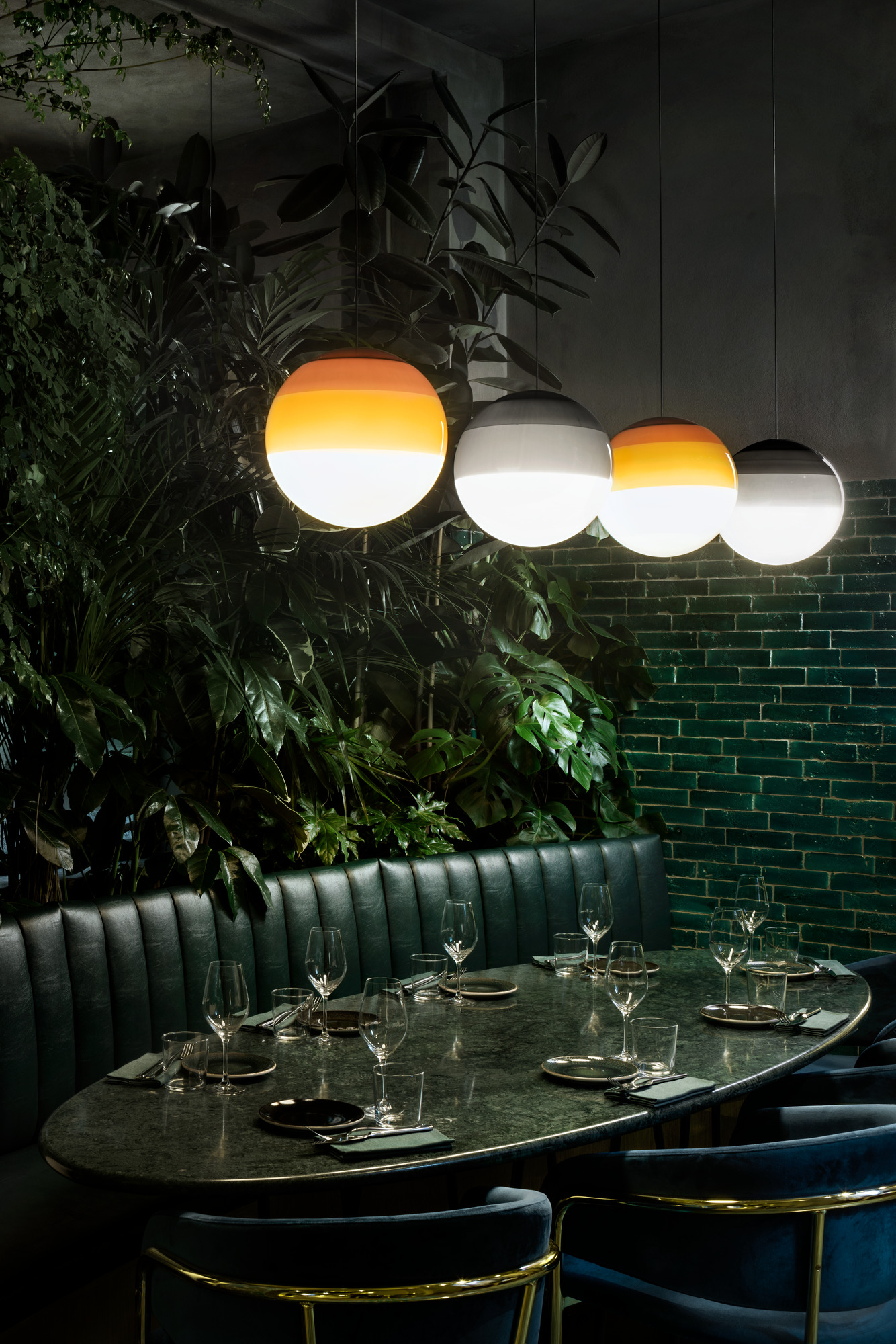 Dipping Light Pendelleuchten in Grün und Orange über einem gedeckten Tisch in einem Restaurant.