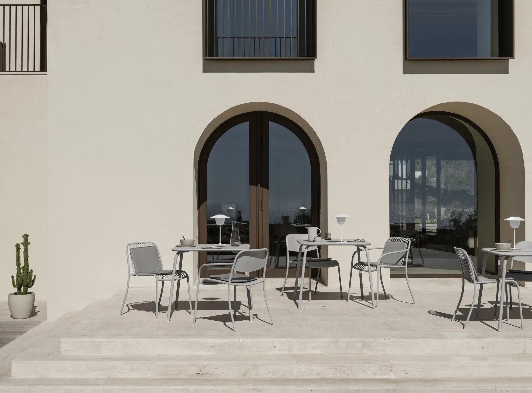 Blomus Yua Chair Outdoor in Silk Gray an Esstischen vor modernem Gebäude.