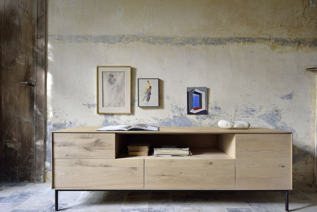 Whitebird TV Möbel von Ethnicraft aus hellem Holz mit Schubladen und Ablageflächen vor rustikaler Wand.