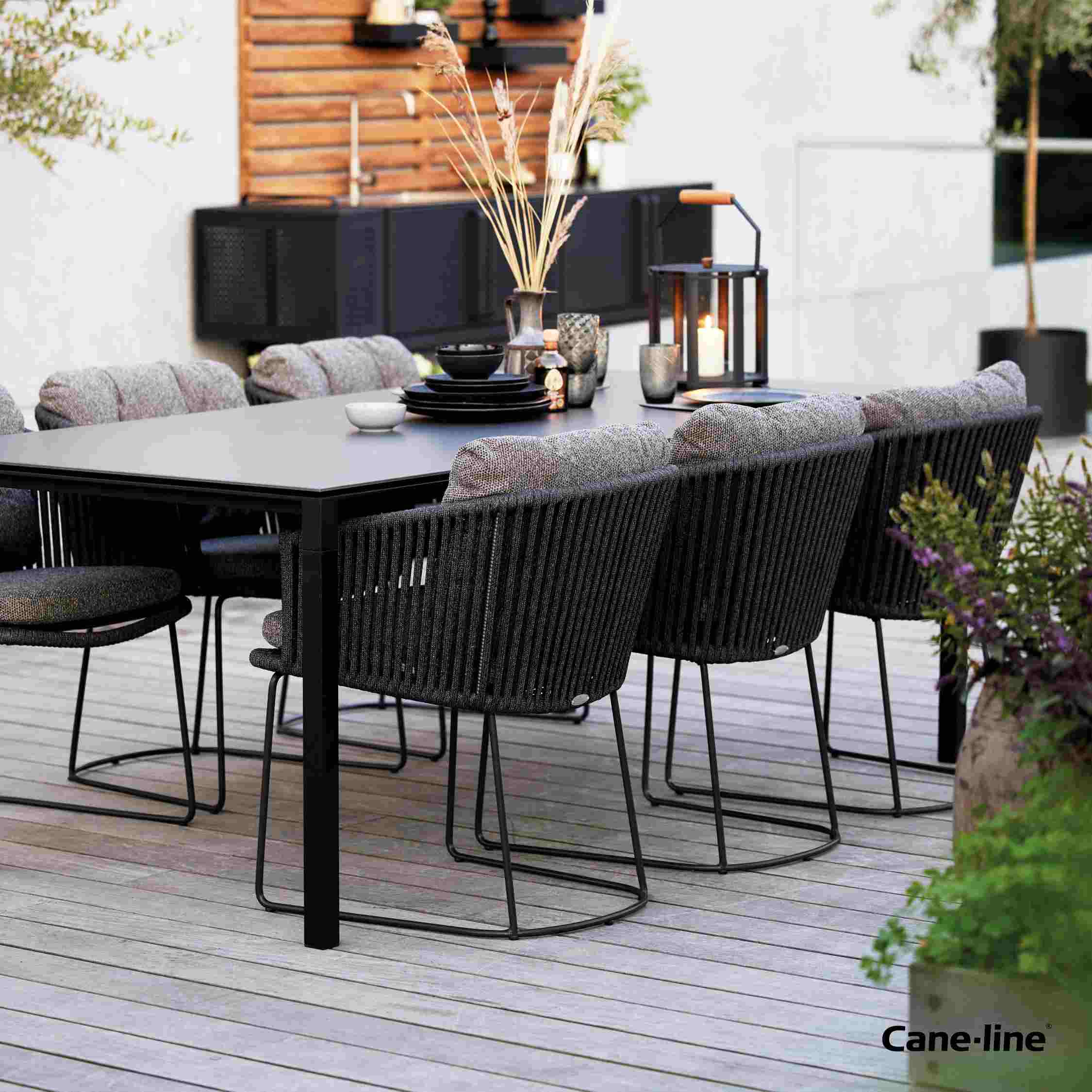 Grauer Cane-Line Moments Stuhl mit Kordelgeflecht und Polster auf einer Terrasse.