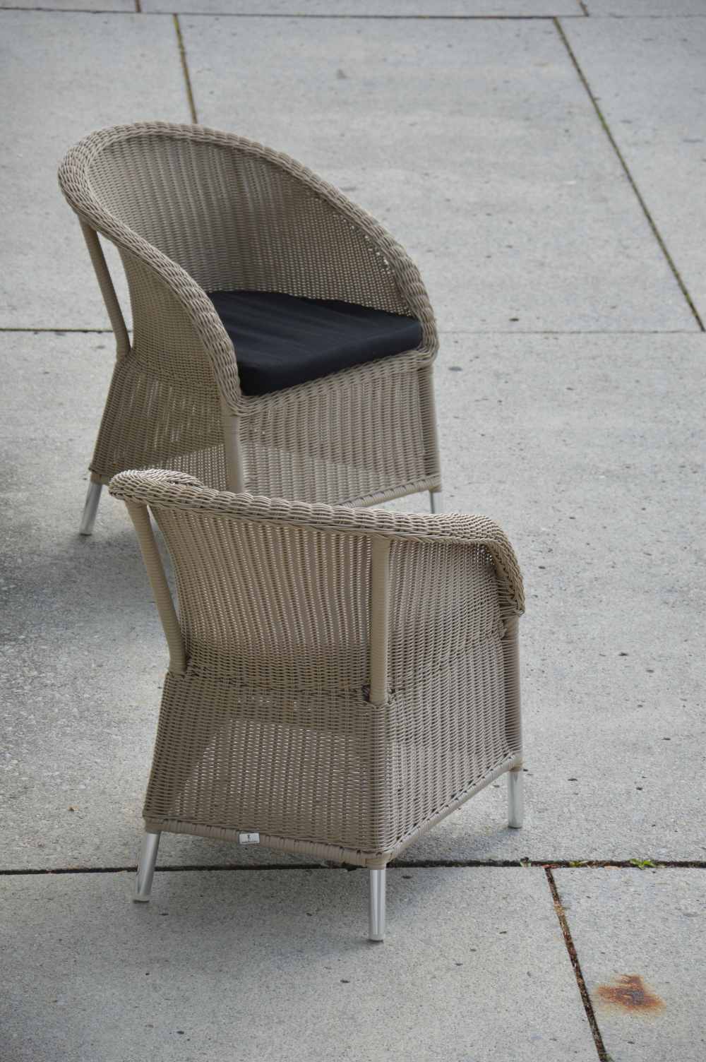 Zwei graue Jan Kurtz Romantik Sessel aus Rattan mit schwarzen Sitzkissen für den Garten.