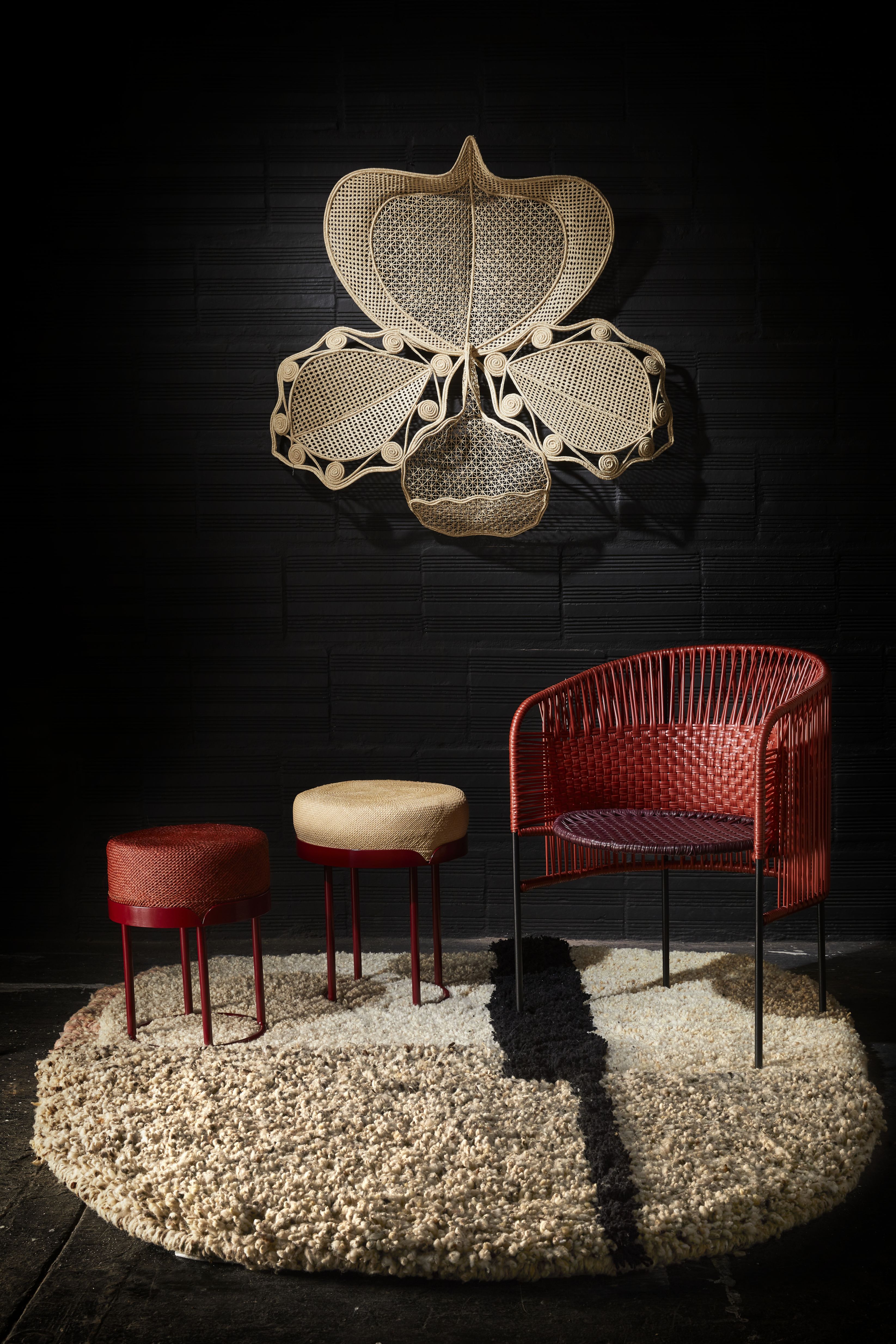 Ames Teppich Nudo large, Wollteppich mit Stühlen und Hockern vor schwarzer Wand.