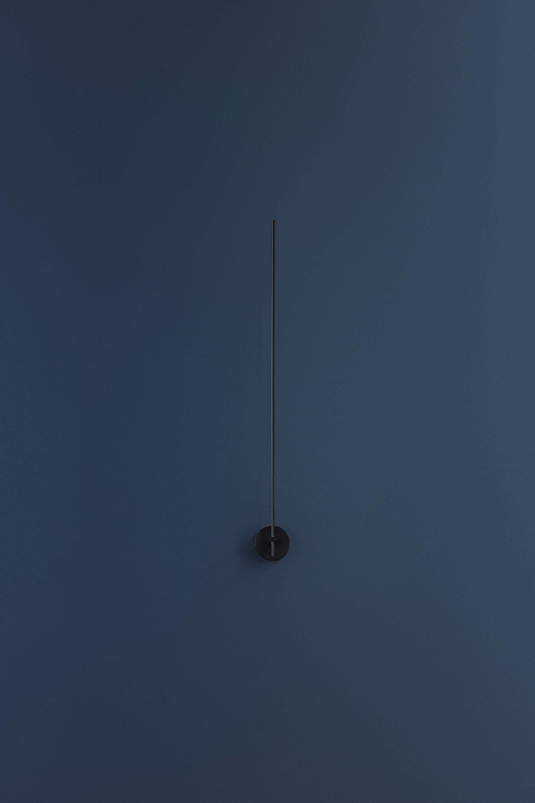 Schwarze Light Stick Wandleuchte von Catellani & Smith vor dunkelblauer Wand. Minimalistisches Design.