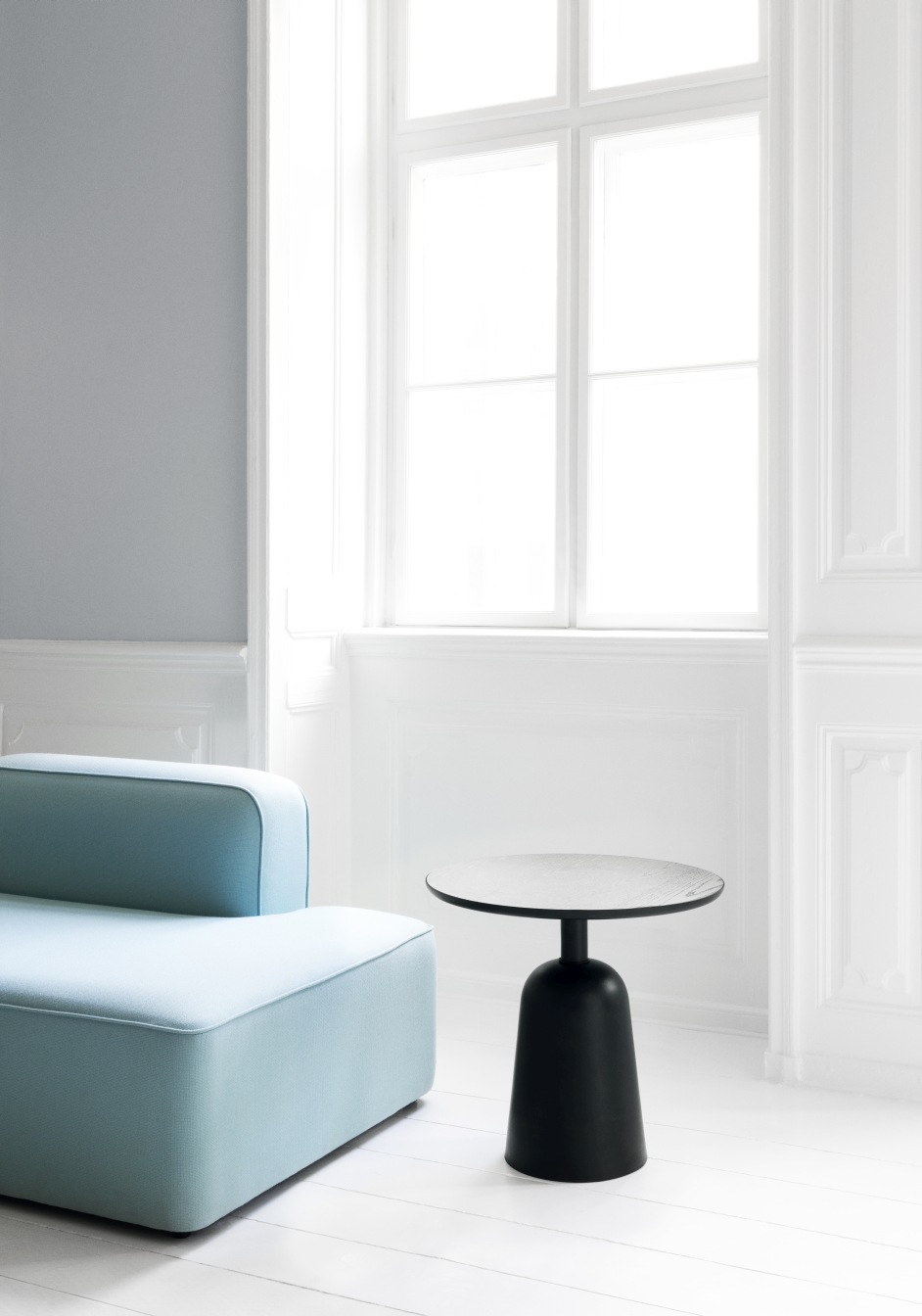 Normann Copenhagen Turn Table Beistelltisch in Schwarz neben hellblauem Sofa in minimalistischem Interieur.