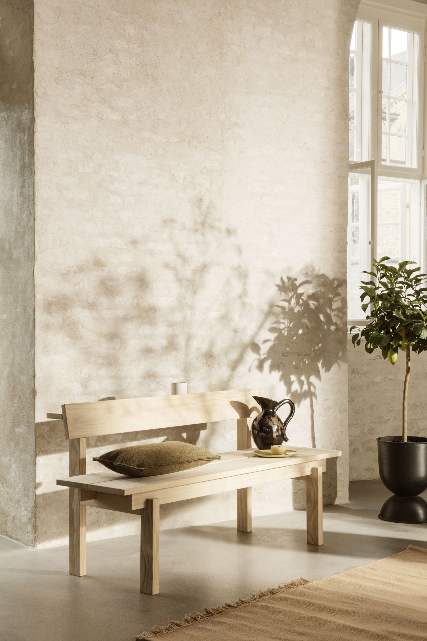 Helle Holzbank, vermutlich Peka Bank, mit Kissen und Dekoration in einem minimalistischen Interieur.