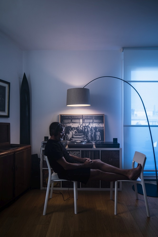 Mann entspannt unter der grauen Twiggy Wood LED Stehleuchte von Foscarini im Wohnzimmer.