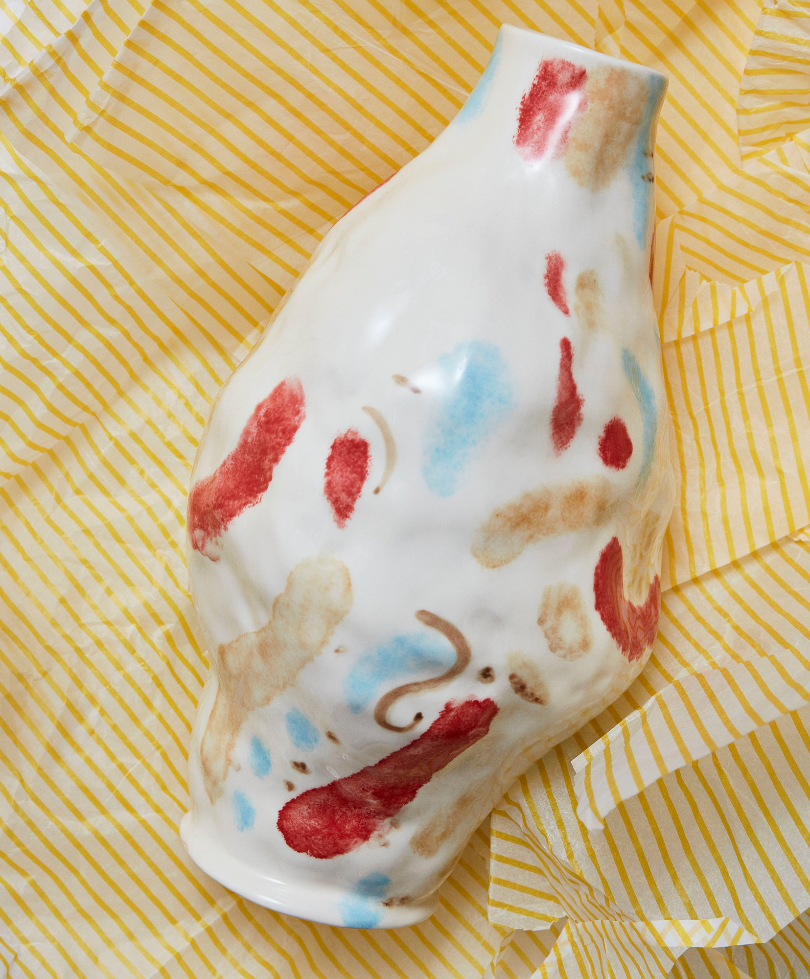 Weiße Jessica Hans Vase von Hay mit abstrakten roten, blauen und braunen Farbakzenten auf gelbem Papier.