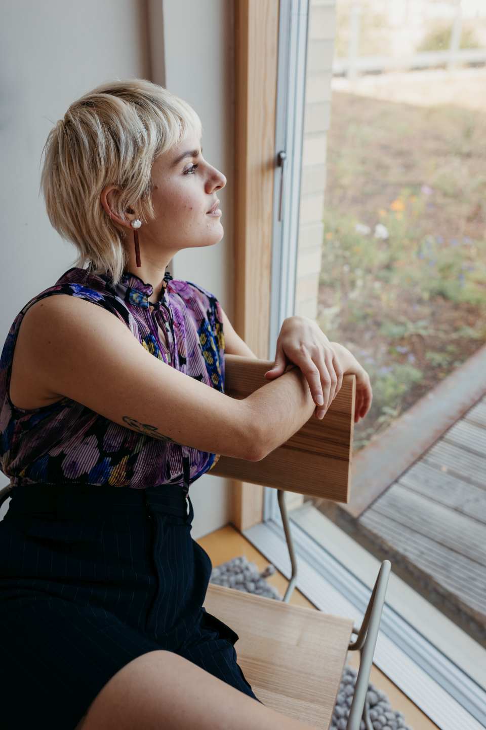 D:008 Loungechair: Frau sitzt entspannt im Sessel mit Armlehnen und blickt aus dem Fenster.