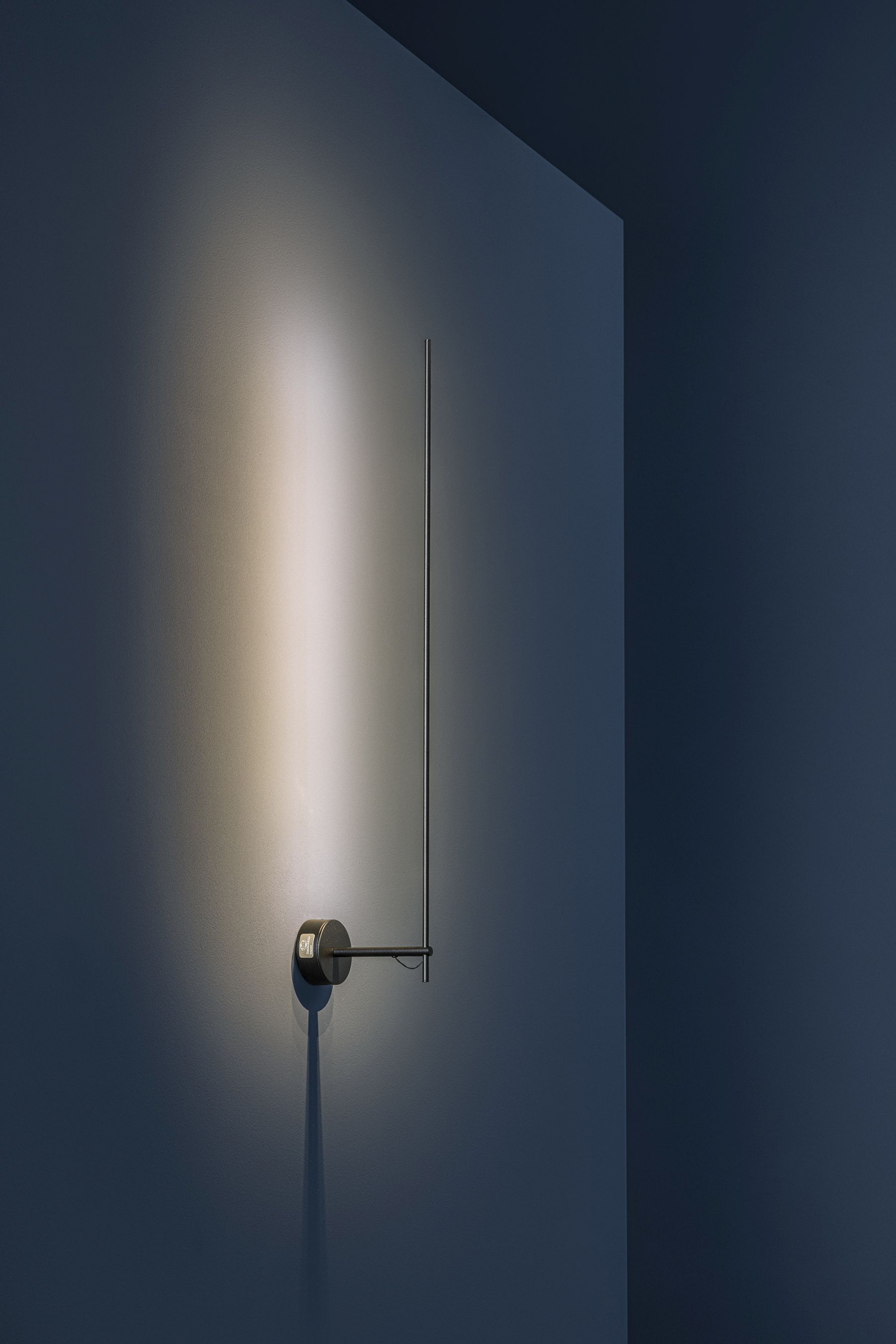 Schwarze Catellani & Smith Light Stick Wandleuchte an blauer Wand, minimalistisches Design, indirekte Beleuchtung.