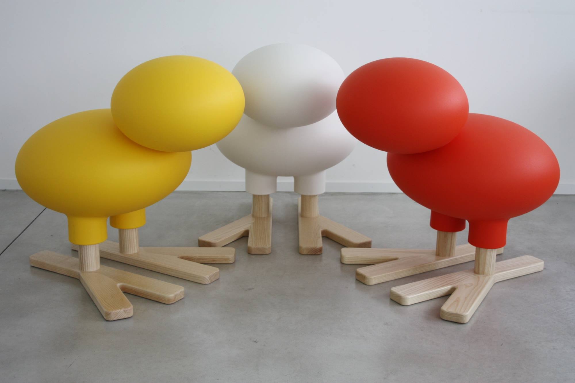 Drei Happy Bird Figuren von Magis in Gelb, Weiß und Rot mit Holzfüßen.