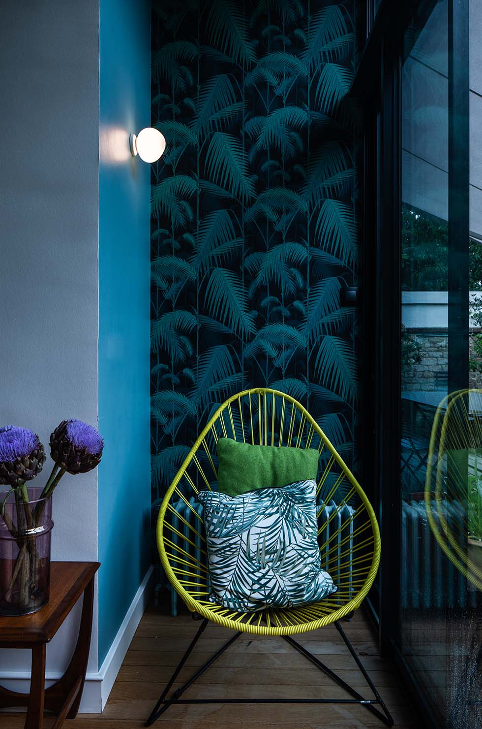 Gregg Wandleuchte von Foscarini, runde Design-Leuchte an blauer Wand, neben Sessel mit Kissen.