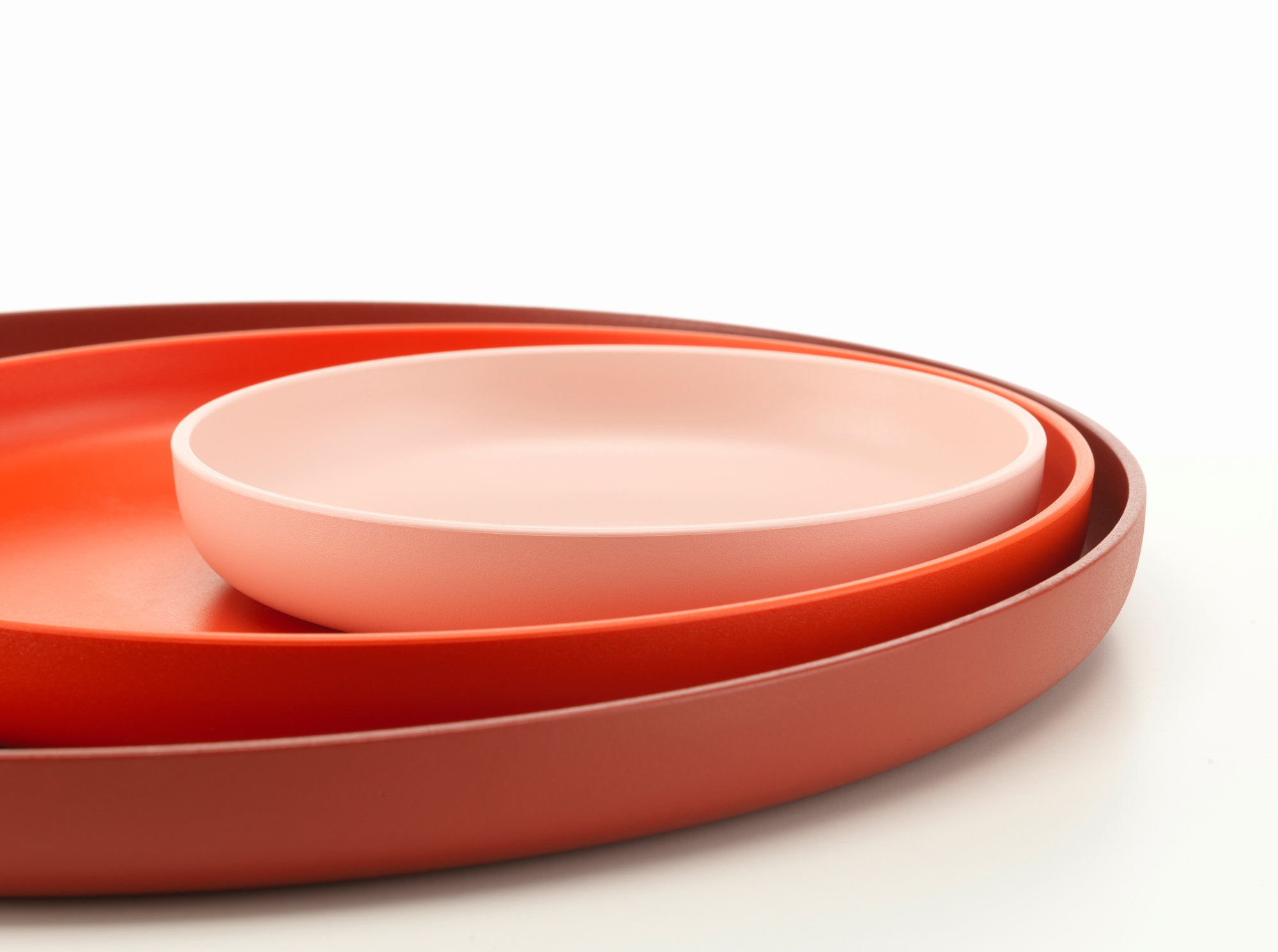 Vitra Trays Tablett-Set: Drei farbige Tabletts in Rosa, Orange und Rot gestapelt.