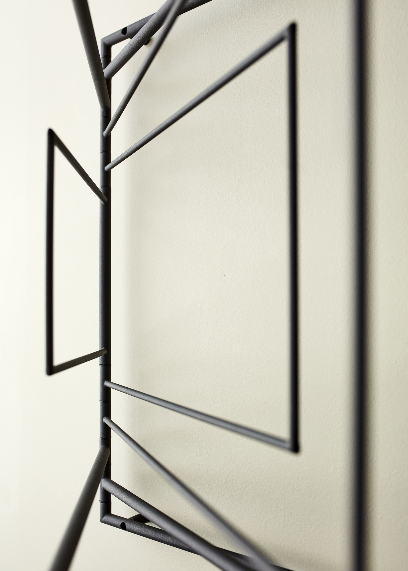 Detailaufnahme der Frame Wandgarderobe: Schwarzes Metallgestell mit geometrischen Formen an einer hellen Wand.