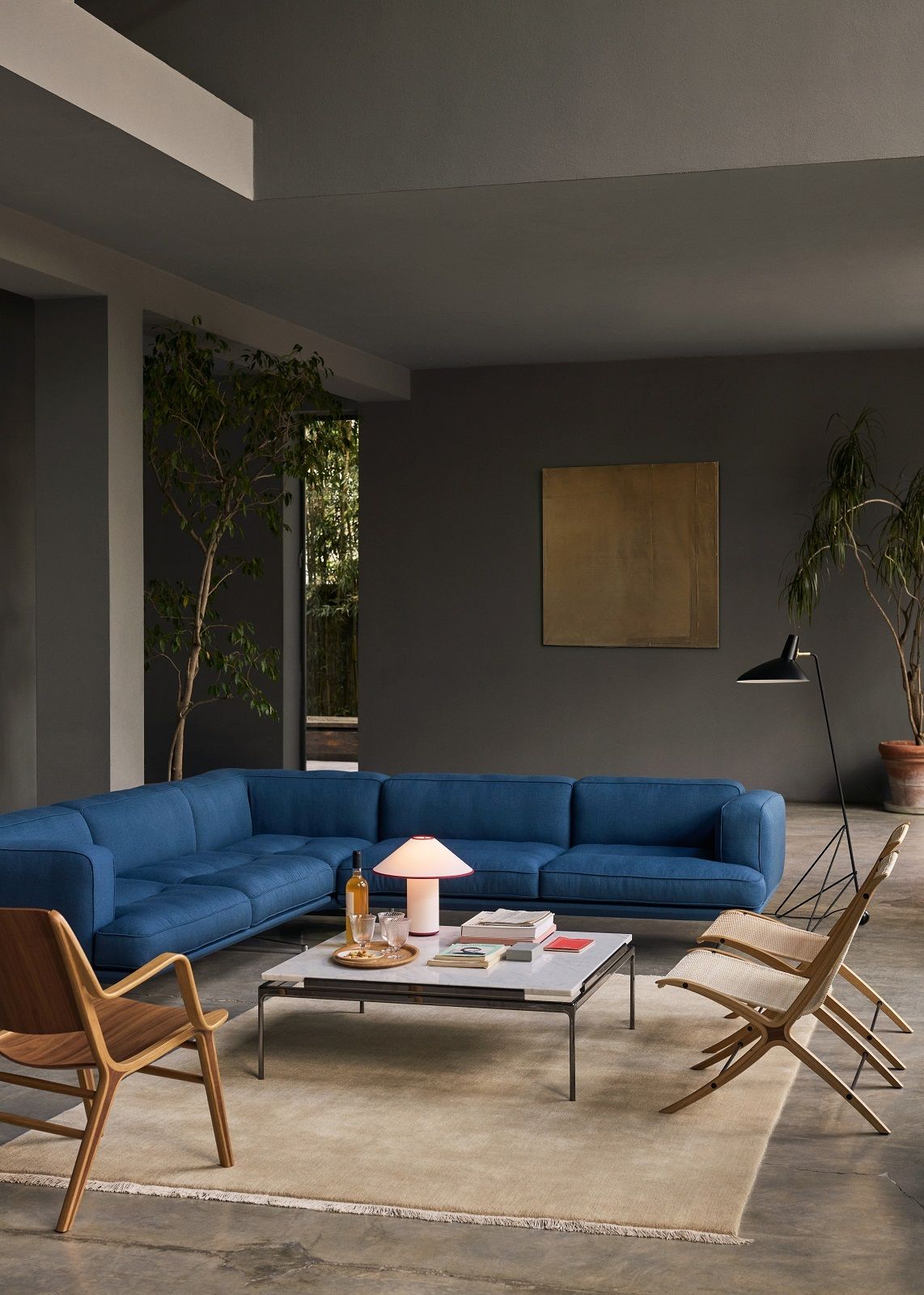 Blaues AndTradition AV41 Sofa in modernem Wohnzimmer mit Teppich, Tisch und Stühlen.