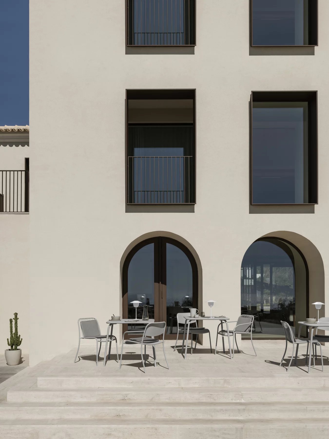 Nahaufnahme von mehreren grauen Yua Wire Stühlen von Blomus im Außenbereich vor einem Gebäude.