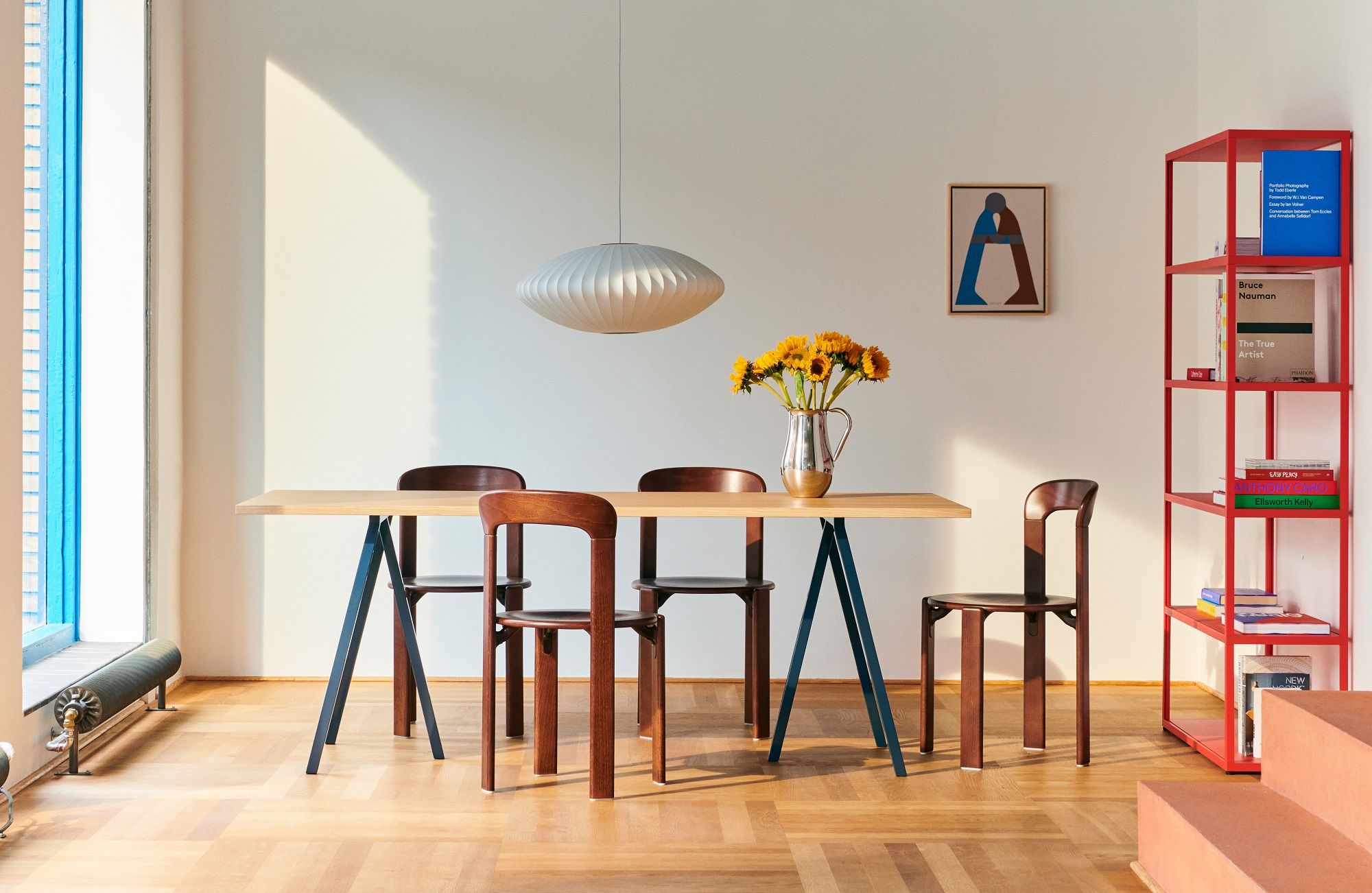 Esszimmer mit Hay Loop Stand Table, Holzstühlen und Sonnenblumen in Vase. Moderner Esstisch.