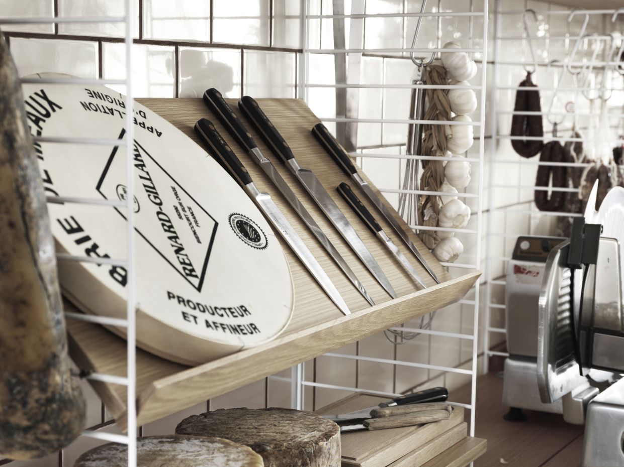 String Regalsystem: Käse, Messer und Knoblauch auf einem Holzregal an einer weißen Wand.