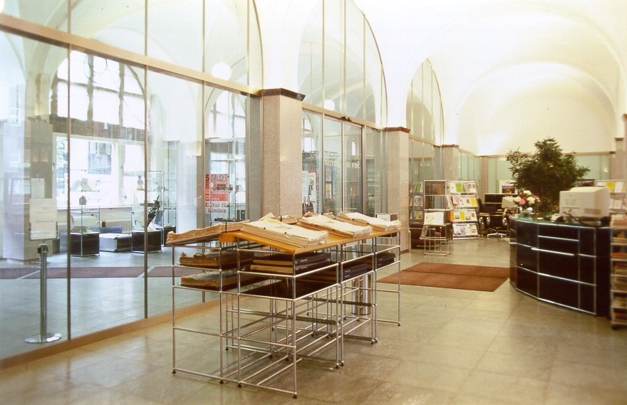 Innenaufnahme eines Ausstellungsraums mit USM Haller Möbeln, darunter ein Stehpult mit Dokumenten.