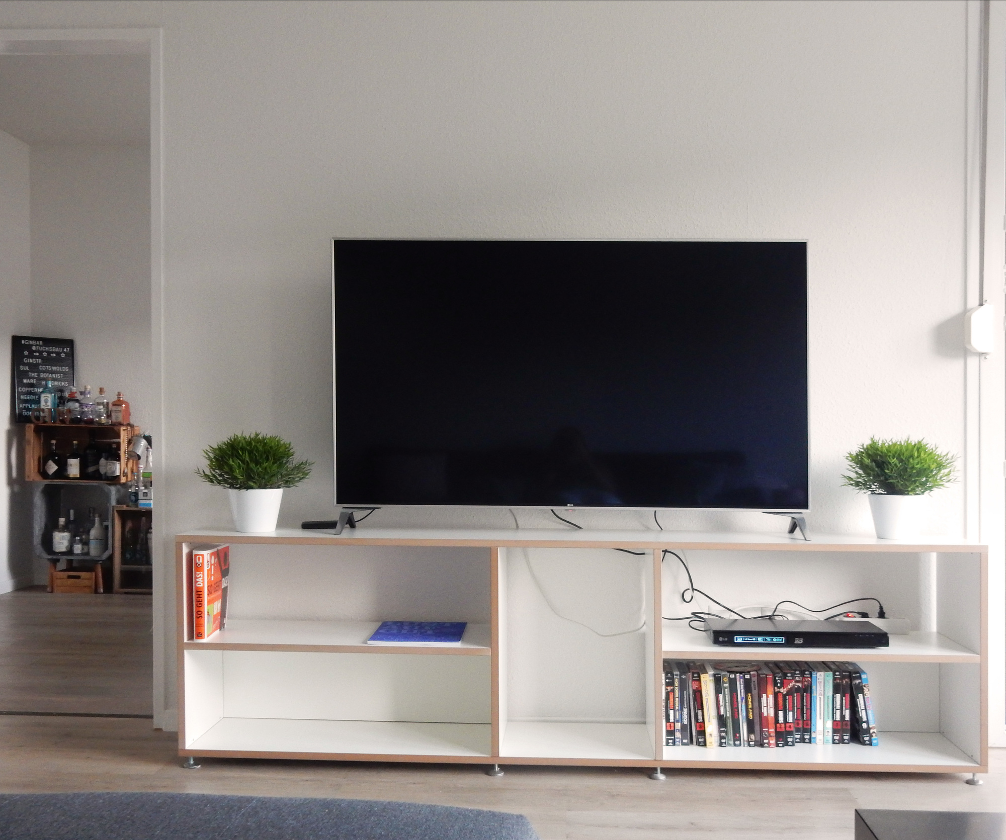 Helles Wohnzimmer mit niedrigem Hanibal Regal von Tojo unter einem Fernseher.