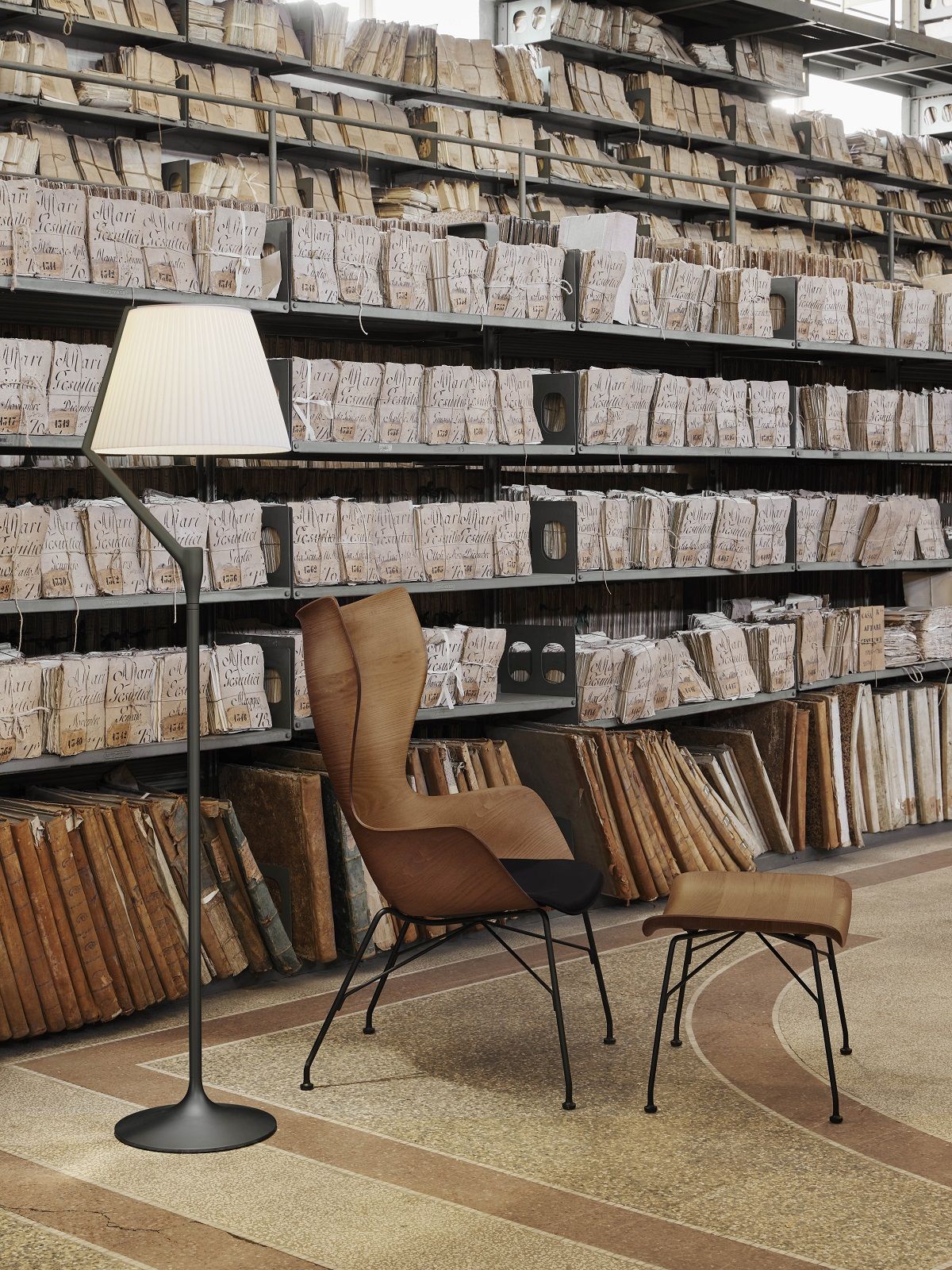 Angelo Stone Stehleuchte von Kartell: Moderne Stehlampe mit weißem Schirm vor Bücherregalen.