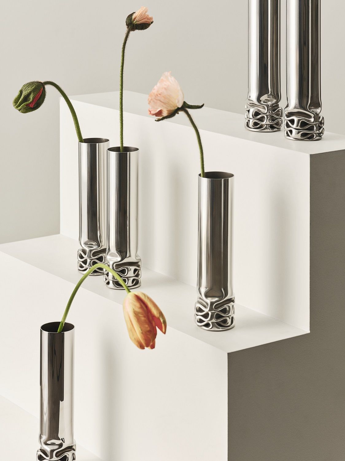 Hydraulic Vase von Design House Stockholm aus poliertem Edelstahl mit zarten Blumen auf weißen Stufen.