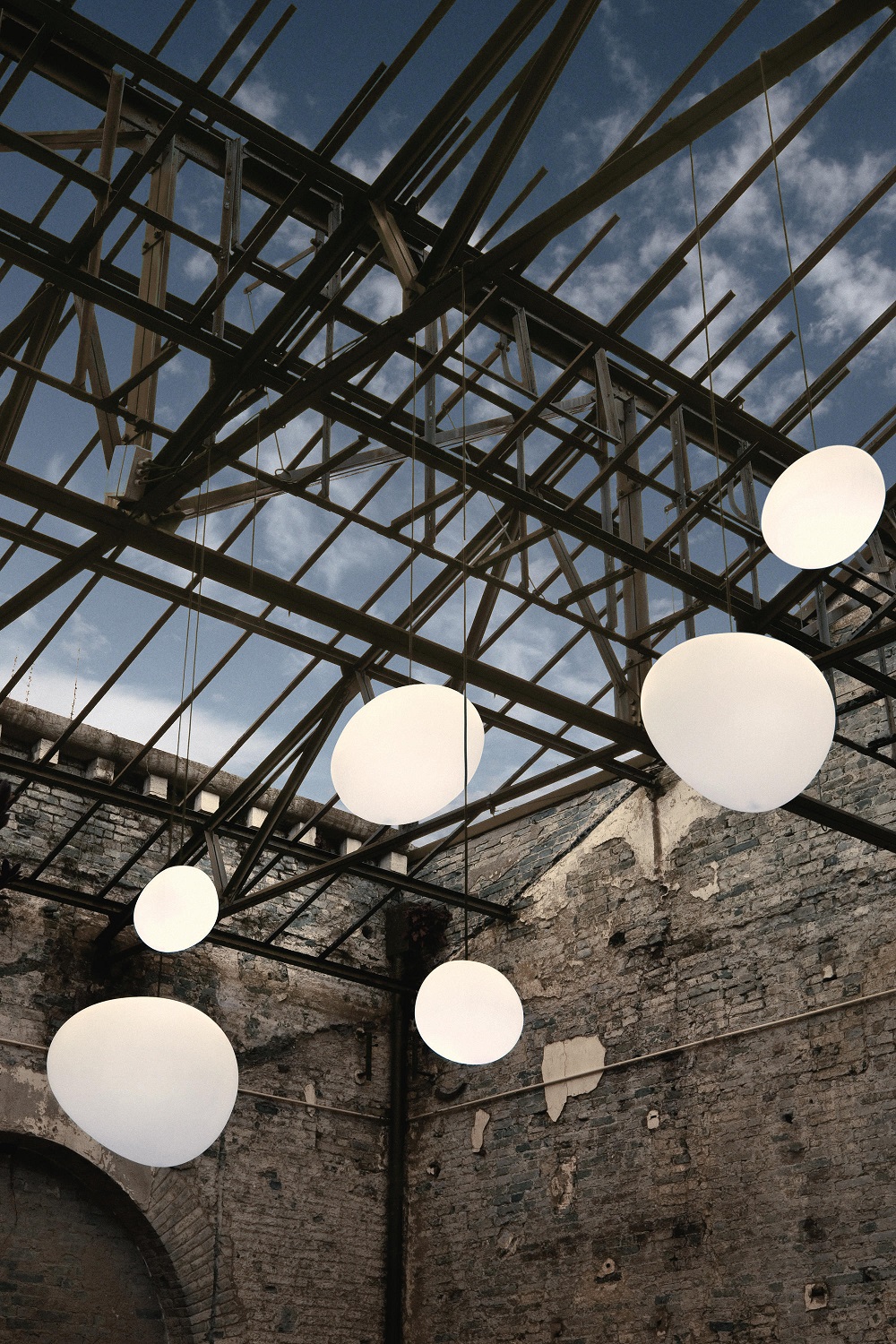 Mehrere weiße Gregg Pendelleuchten von Foscarini hängen unter einem offenen Dach. Outdoor-Beleuchtung.