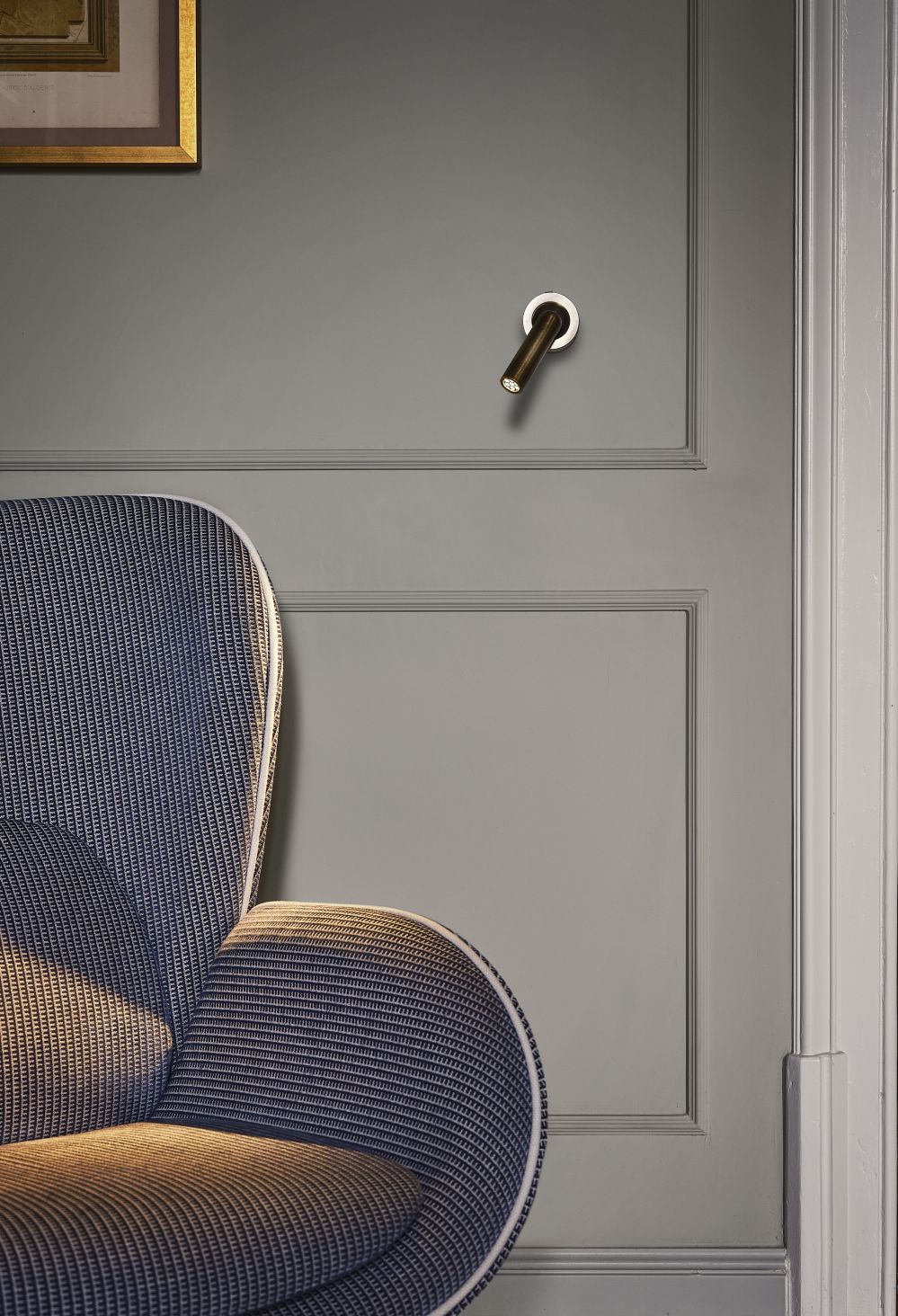 Nahaufnahme der Ledtube A Wandleuchte von Marset an grauer Wand, neben Sessel.