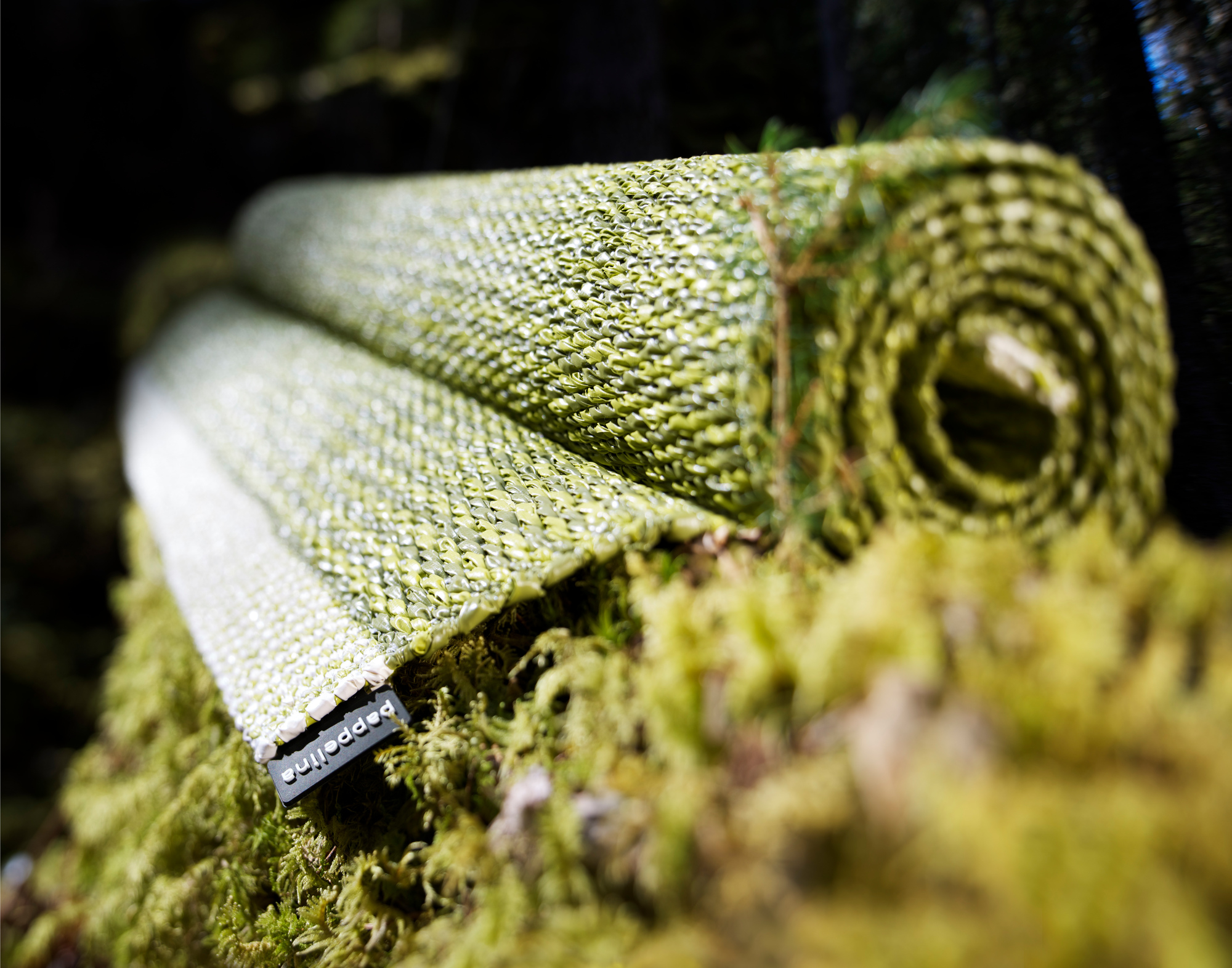 Aufgerollter Pappelina Mono Kunststoffteppich in Grün-Weiß, ideal für drinnen und draußen.