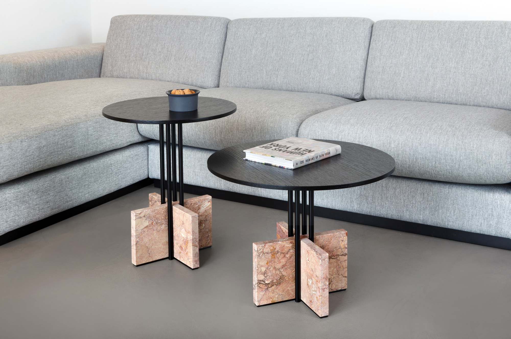 Zwei Gravity Table Beistelltische mit Marmorfuß und schwarzer Tischplatte neben einem grauen Sofa.