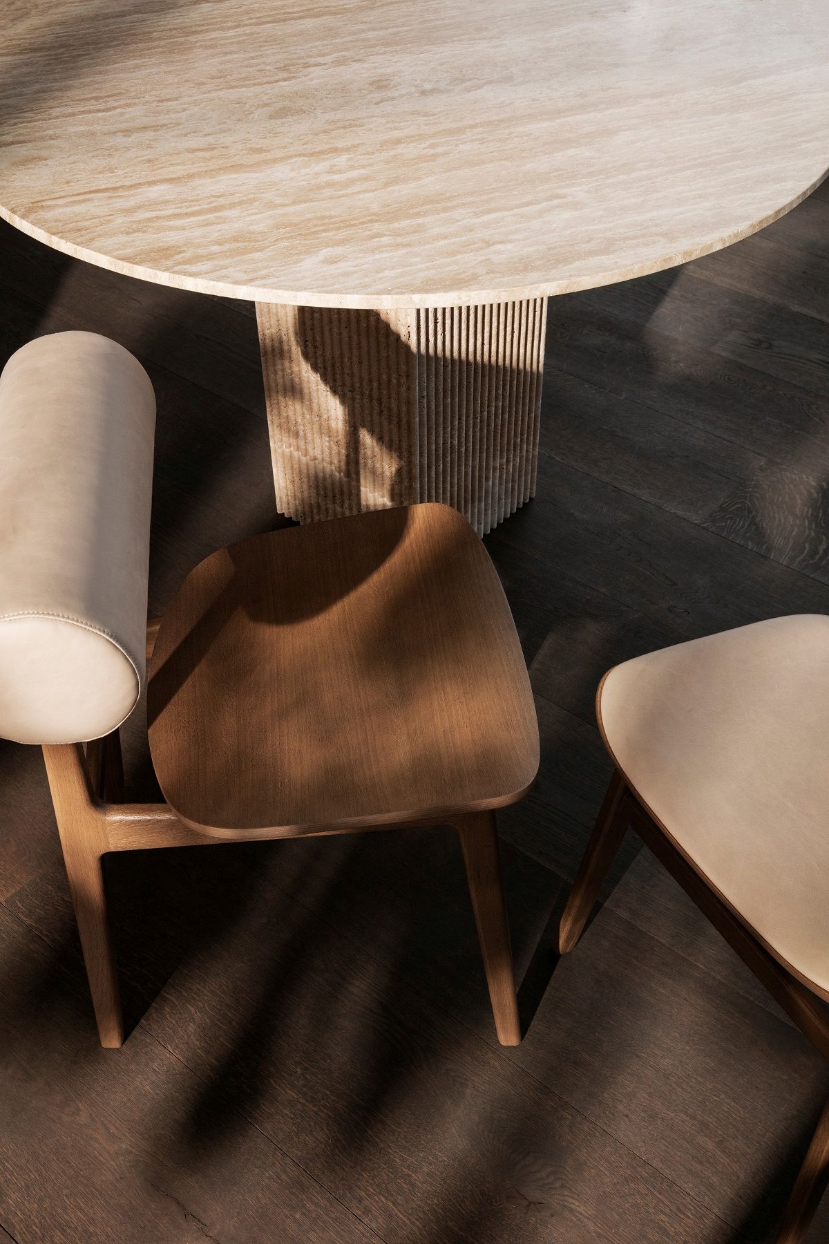 Detailaufnahme des NORR11 Soho Esstischs mit Travertin-Tischplatte und Holzstühlen auf dunklem Holzboden.