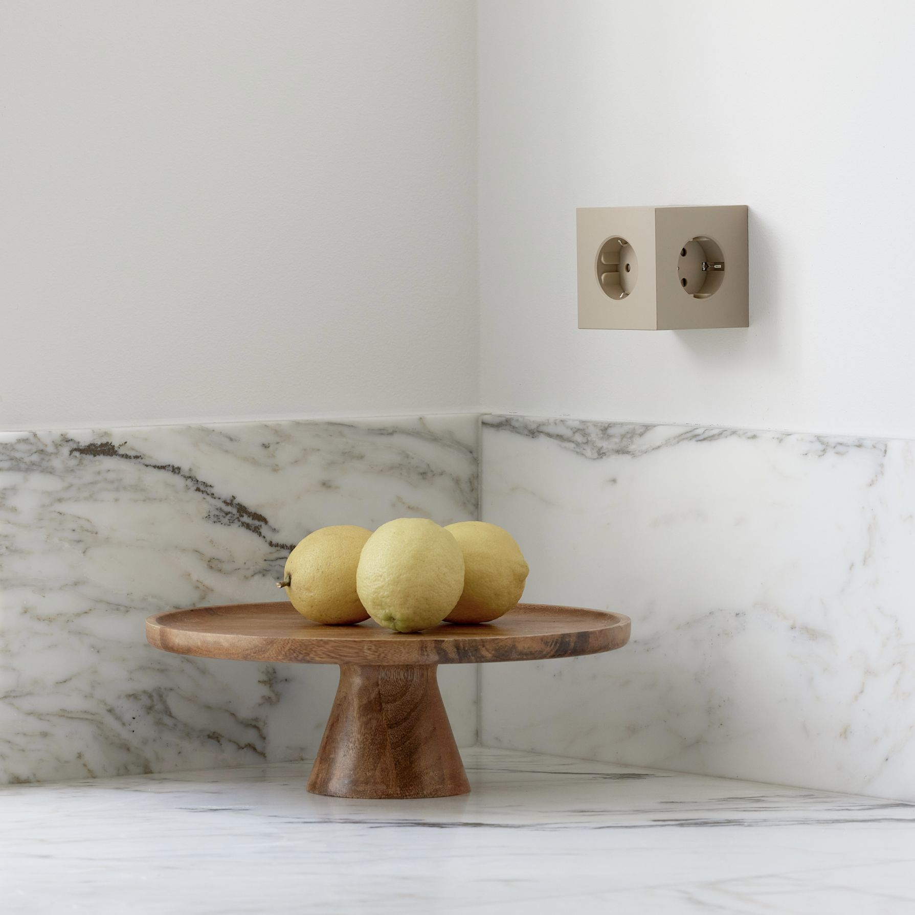 Sandfarbener Avolt Square 2 Steckdosenwürfel mit USB-C an der Wand, Zitrone auf Holztablett.