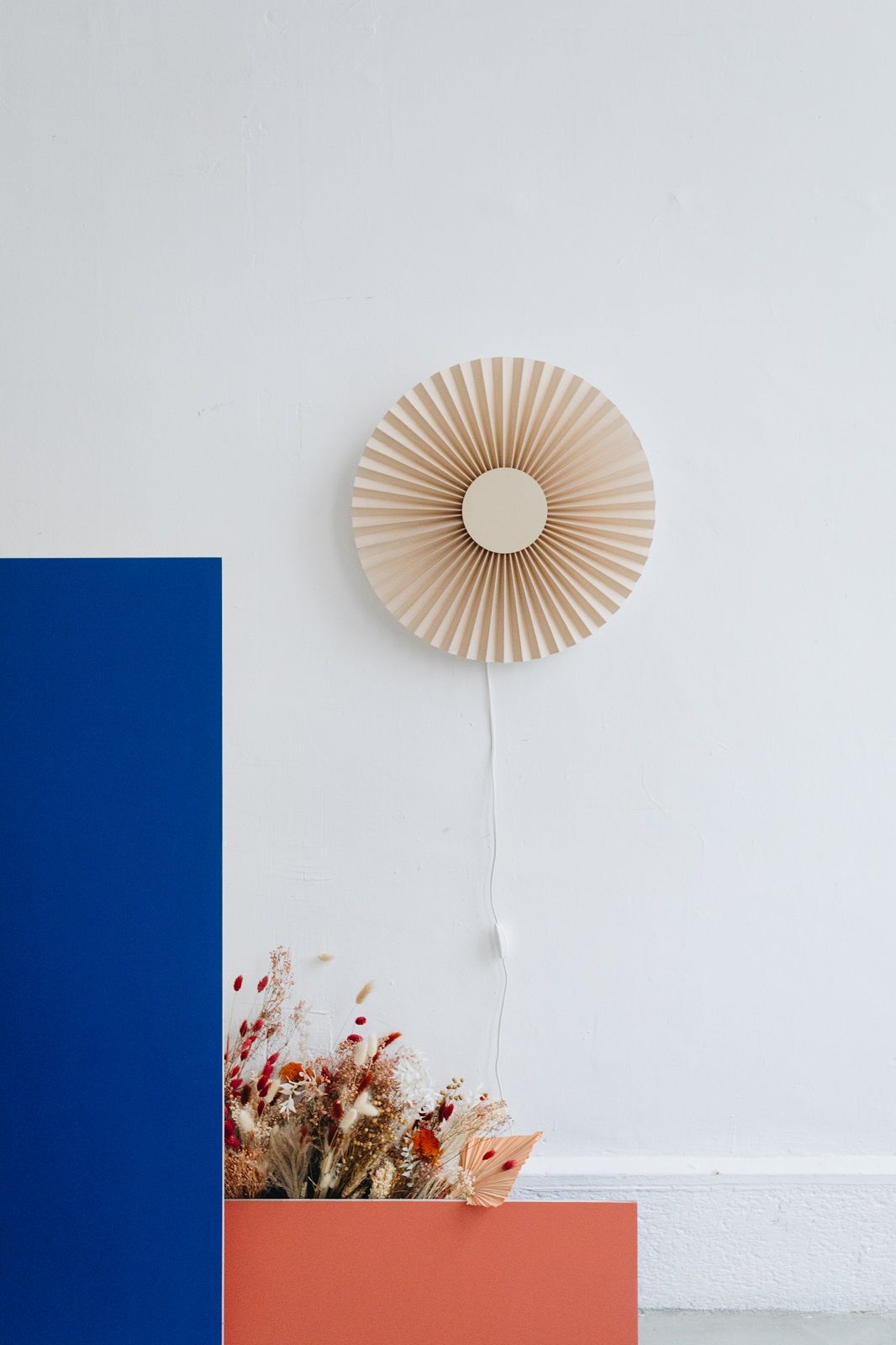 Beige Carmen Wandleuchte von Hartô an weißer Wand, mit Trockenblumen im Vordergrund.