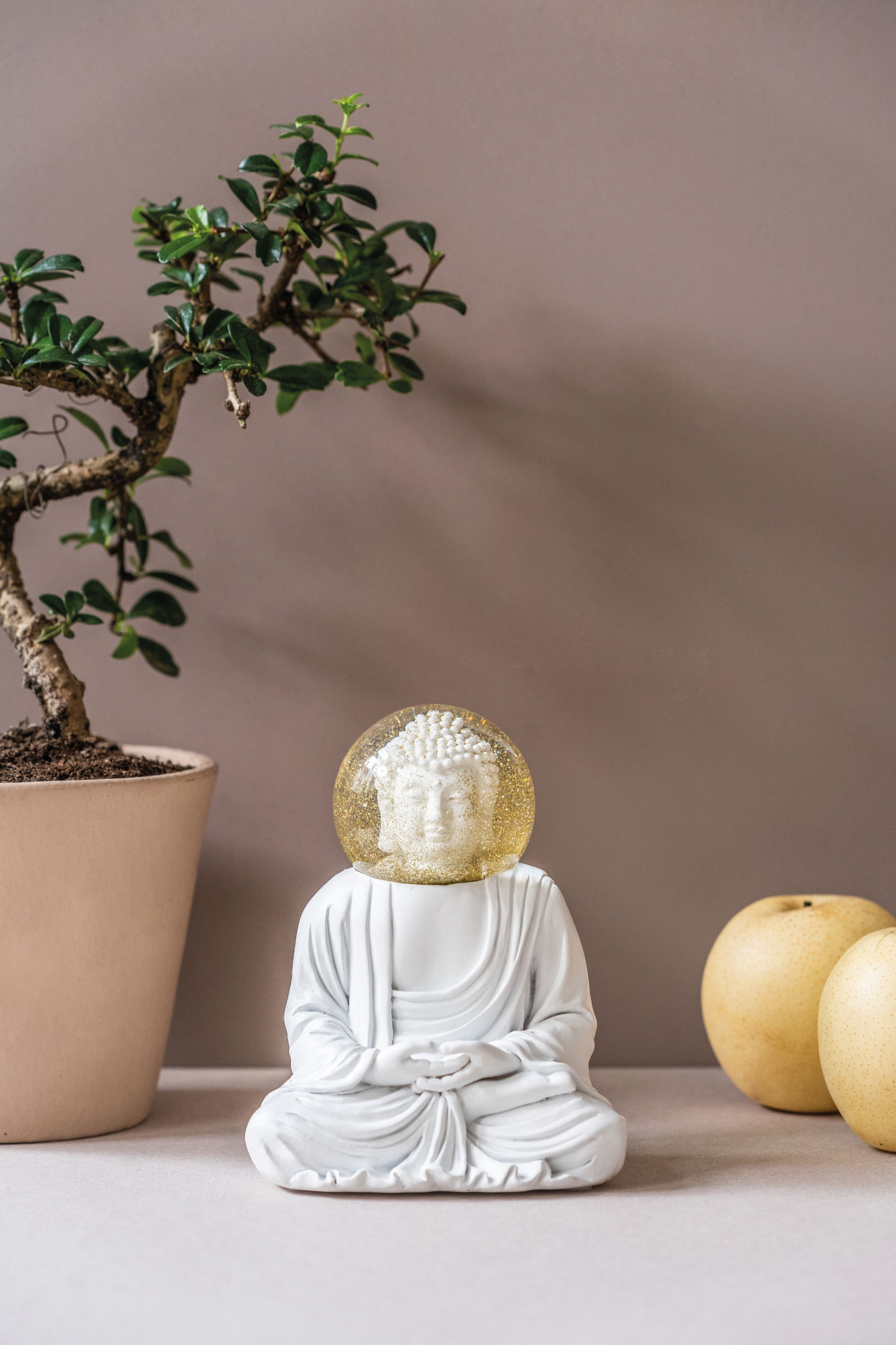 Summerglobes Buddha Glitzerkugel: Weiße Buddha Figur mit goldener Glitzerkugel, Dekoration mit Bonsai und Birnen.