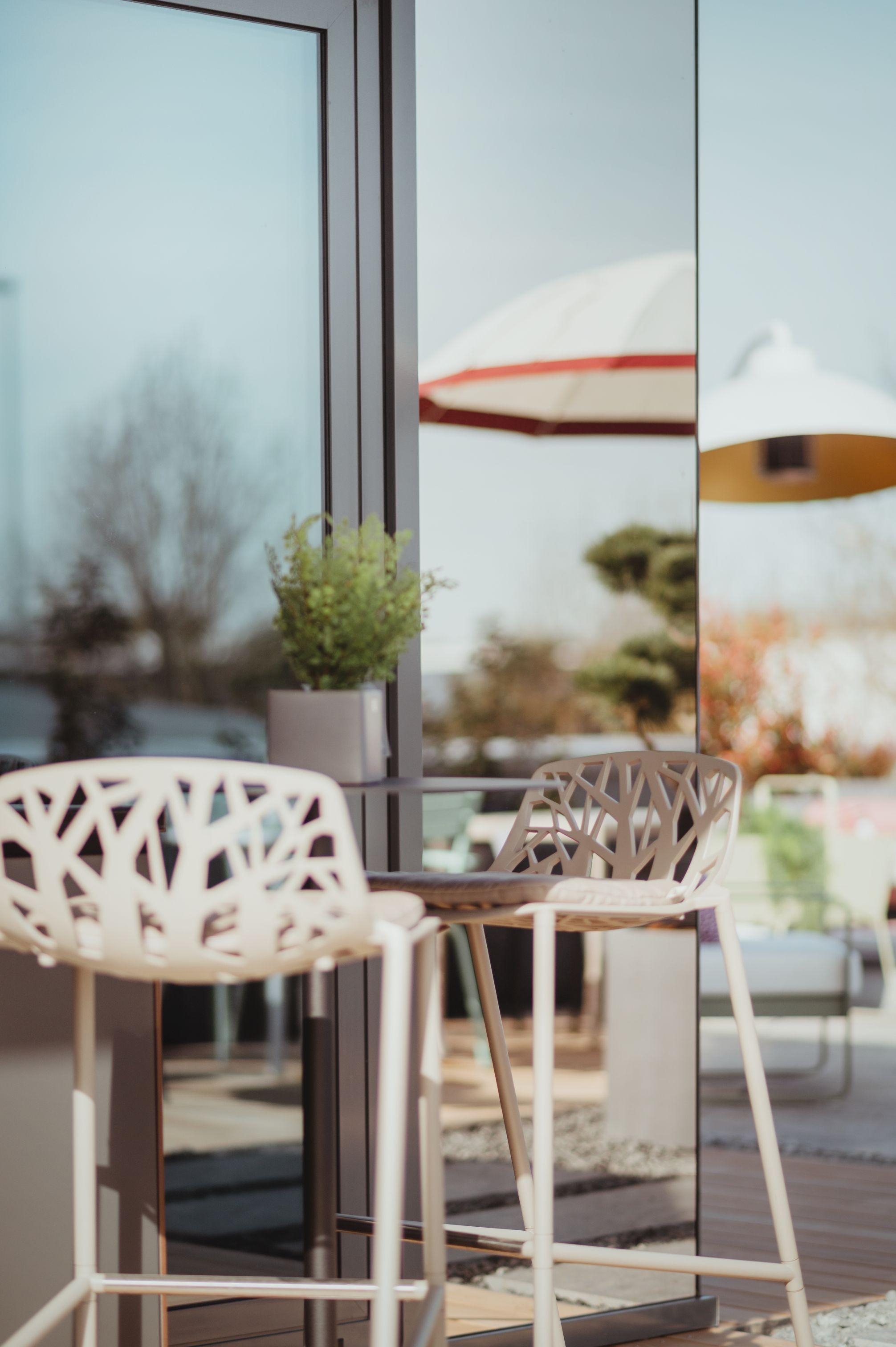 Zwei weiße Forest Barhocker von Fast Outdoor vor einer Glasfassade. Moderne Gartenmöbel.