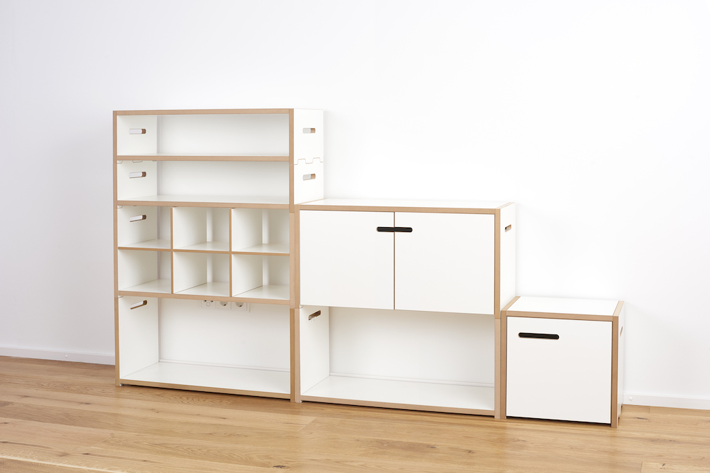 Tojo Halbstark Regalsystem: Weißes, modulares Regal mit Fächern, Schrankelementen und Schublade auf hellem Holzboden.