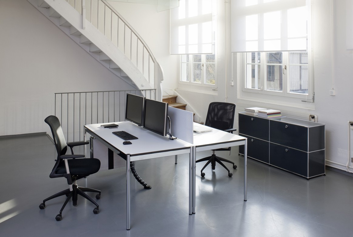 Heller Büroraum mit zwei USM Haller Tischen in Weiß, Bürostühlen, Computern und USM Sideboard.
