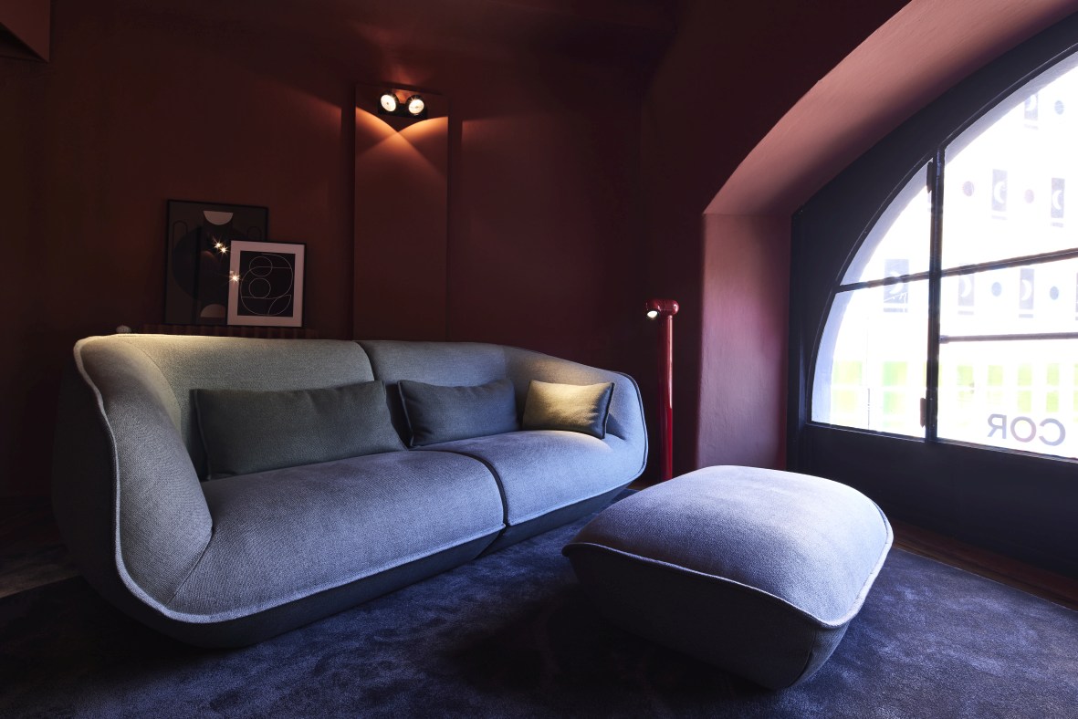 Graues Nook Sofa von Cor mit passendem Hocker in modernem Wohnzimmer Ambiente. Bequeme Polstermöbel.