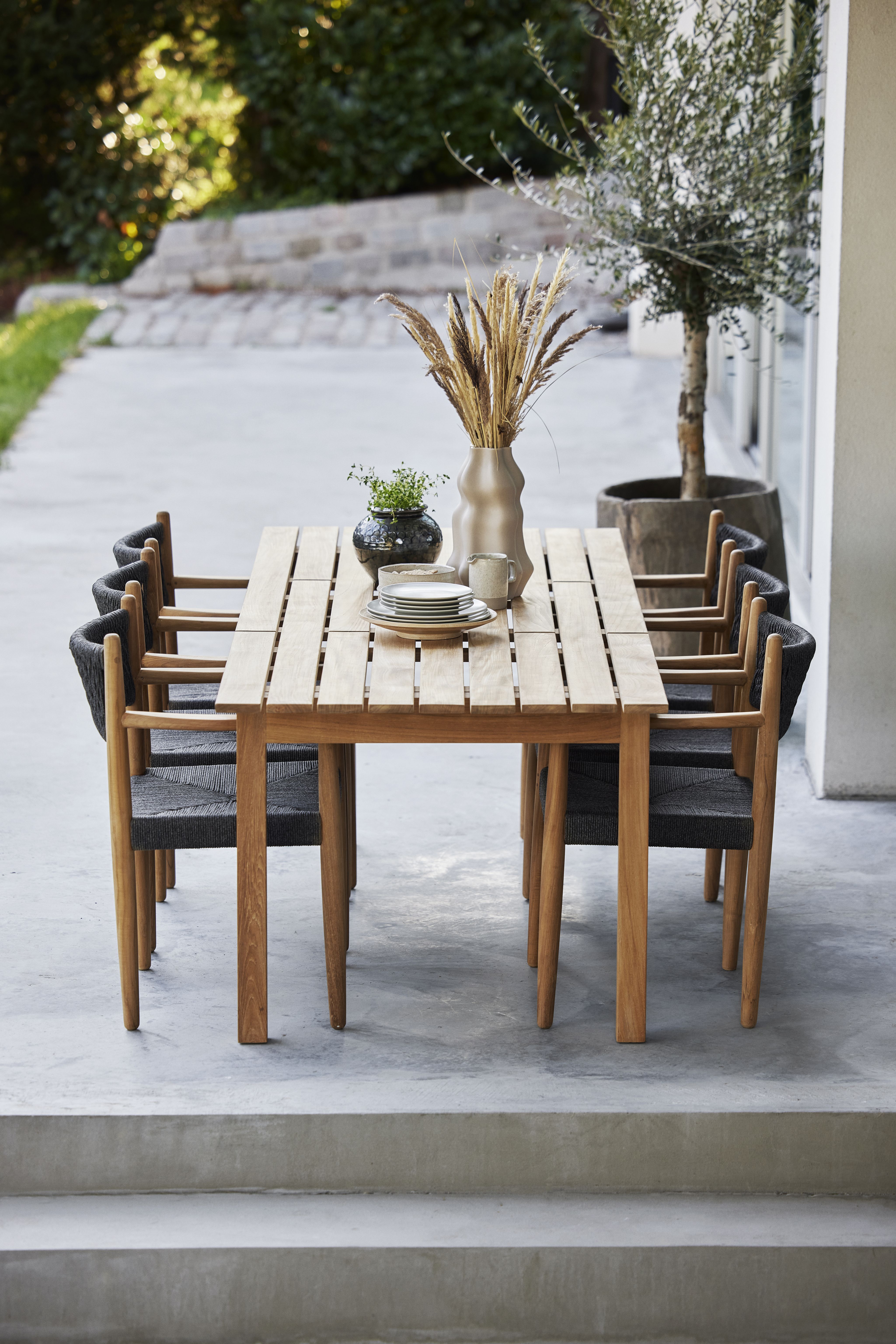 Grace Esstisch von Cane-Line aus Teakholz mit sechs Stühlen und Tischdeko im Außenbereich.