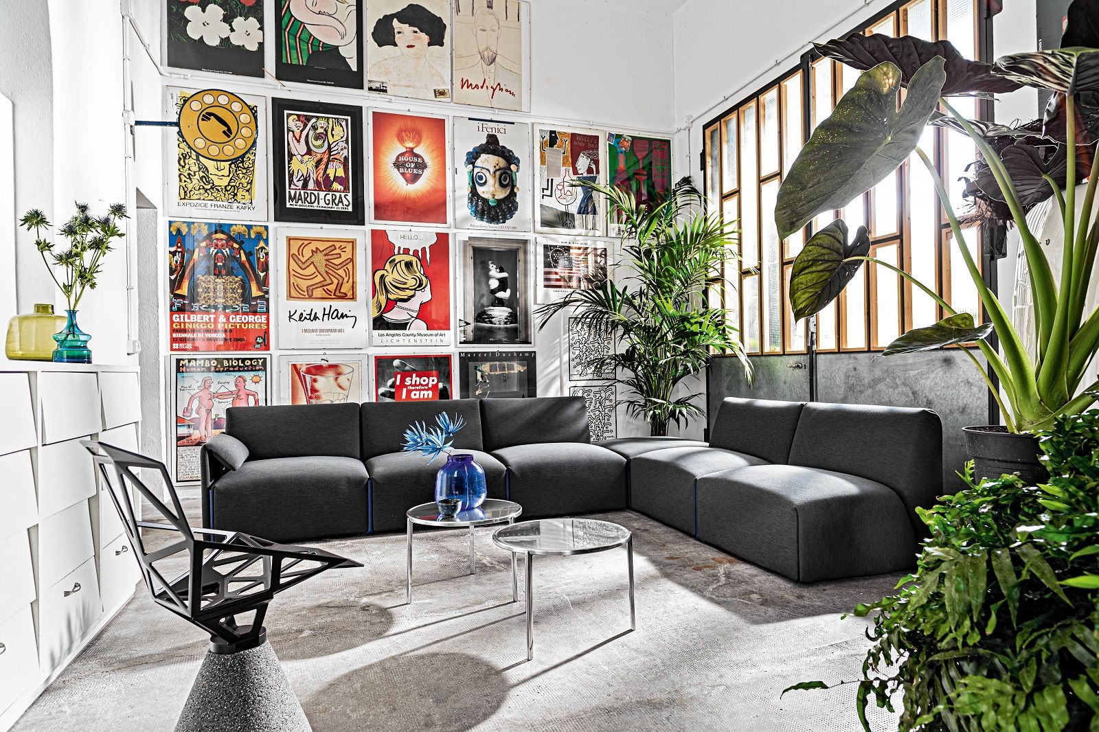 Wohnzimmer Interieur mit Magis Tambour Beistelltisch aus transparentem Kunststoff neben grauer Couch und Zimmerpflanzen.