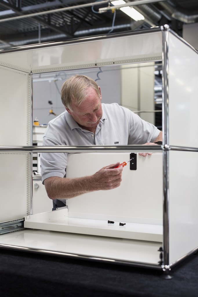 Mann montiert weißen USM Haller Schrank mit Schraubenzieher, modulare Möbel für Büro und Zuhause.